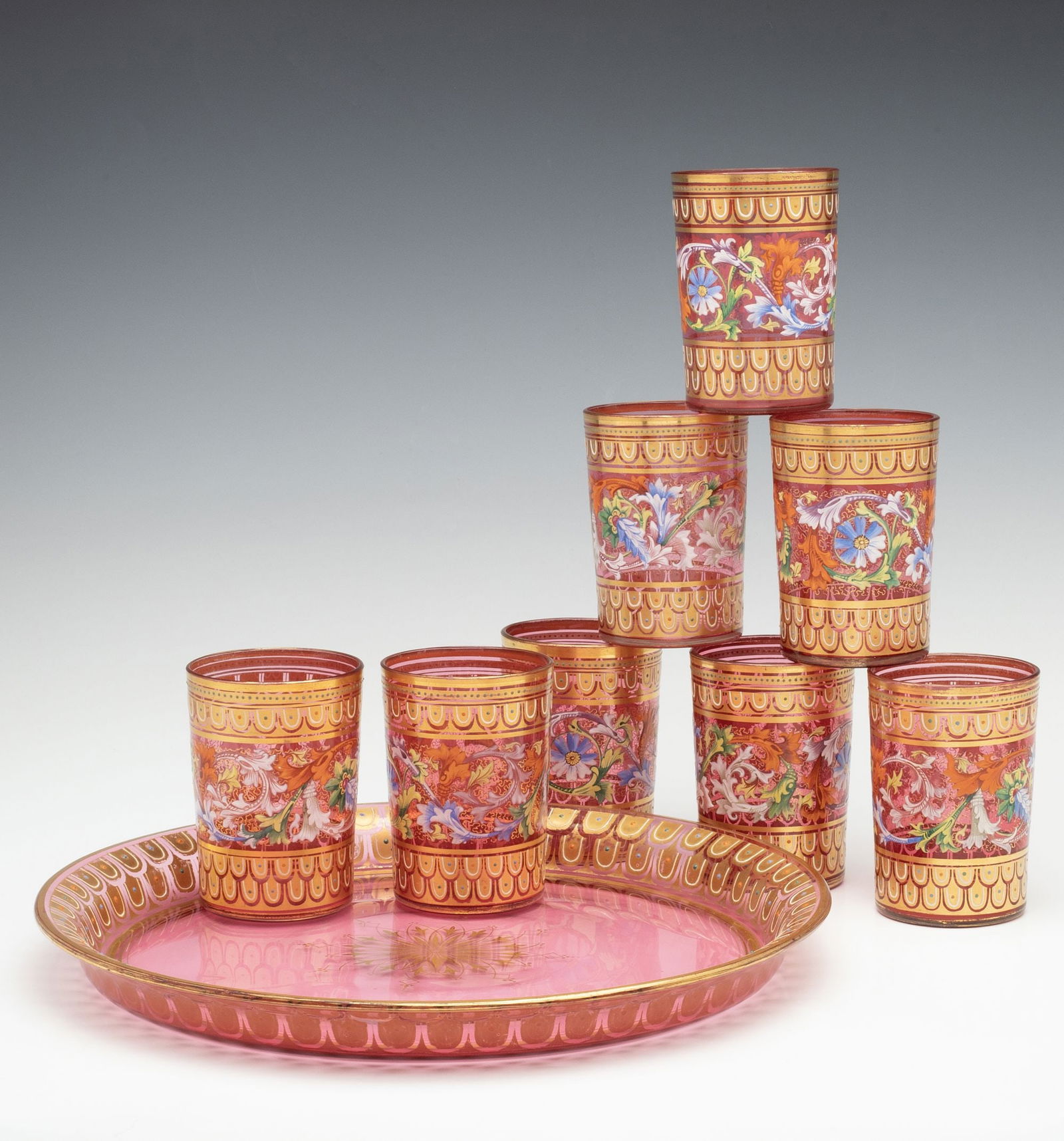 EIGHT MOSER GILT AND ENAMELED CRANBERRY TUMBLERS W/TRAY: Ludwig Moser Late 19th Century Each piece is decorated in bands of swirling, multi-colored foliate relief enamels alternating with bands of overlapping gilt fish scale designs, each scale centered by