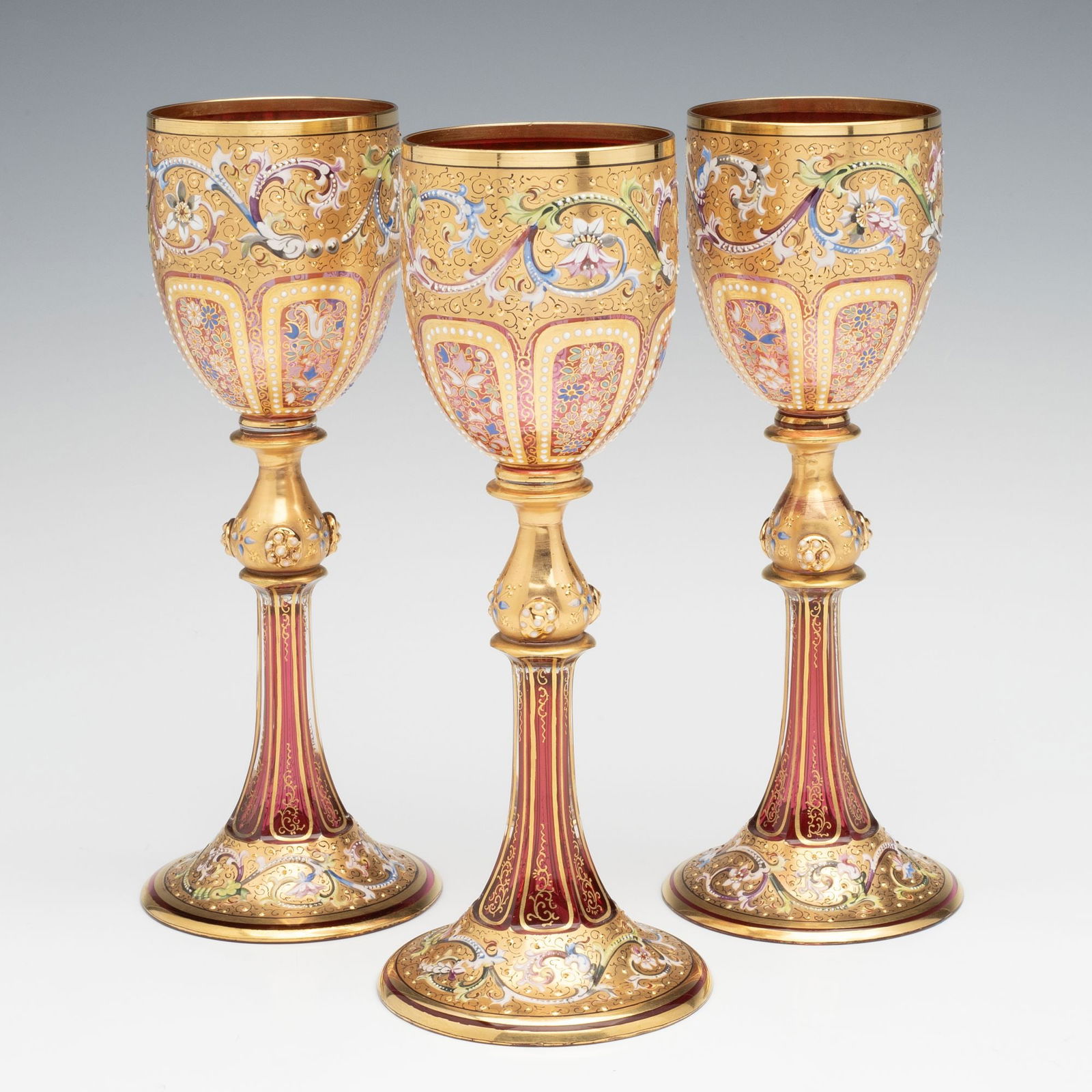 EXCEPTIONALLY FINE MOSER GILT & ENAMELED WINE GOBLETS: Ludwig Moser Late 19th Century Each elegant and unusually elaborate wine goblet with richly gilded bowl is decorated by a band of swirling acanthus in colorful enamels, as found on many Moser art glas