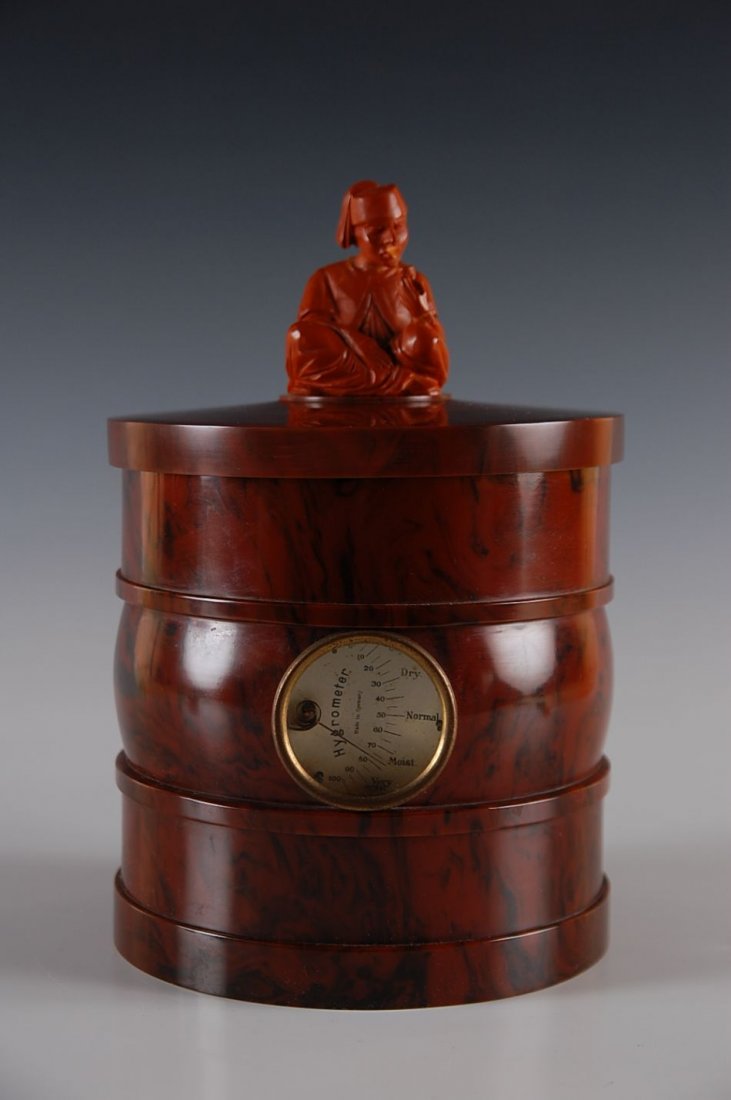 CATLIN BAKELITE HUMIDOR WITH HYGROMETER CIRCA 1940: Topped by a Turkish smoking figure, measures.... A printed disclaimer on the base states 'This imported article of synthetic phenolic resin was manufactured by a foreign concern in no way connected wi