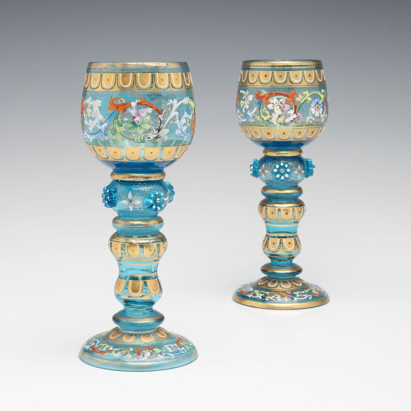 MOSER ELECTRIC BLUE GILT AND ENAMEL WINE GOBLETS: Ludwig Moser Early 20th Century Each goblet has a bulbous bowl encircled by bands of gold lappets and a colorful enamel acanthus scroll. Each bowl is supported by a hollow stem of flaring and waisted
