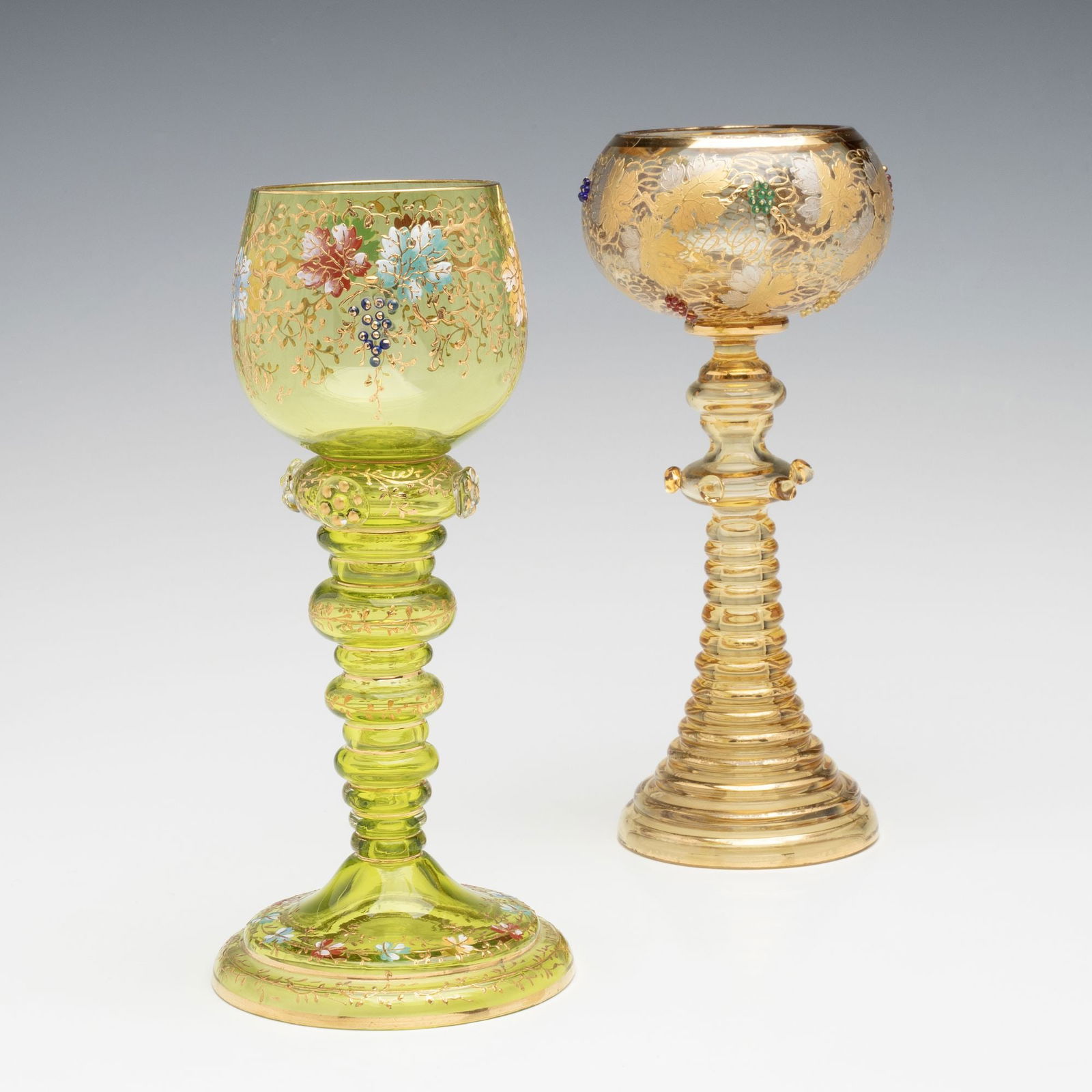 TWO LUDWIG MOSER WINE GOBLETS WITH GLASS BEAD CLUSTERS: Ludwig Moser Early 20th Century Each ornate goblet has enamel decoration accented by applied clusters of glass bead grapes and is raised on an ornate, shaped, hollow glass stem with applied glass prun