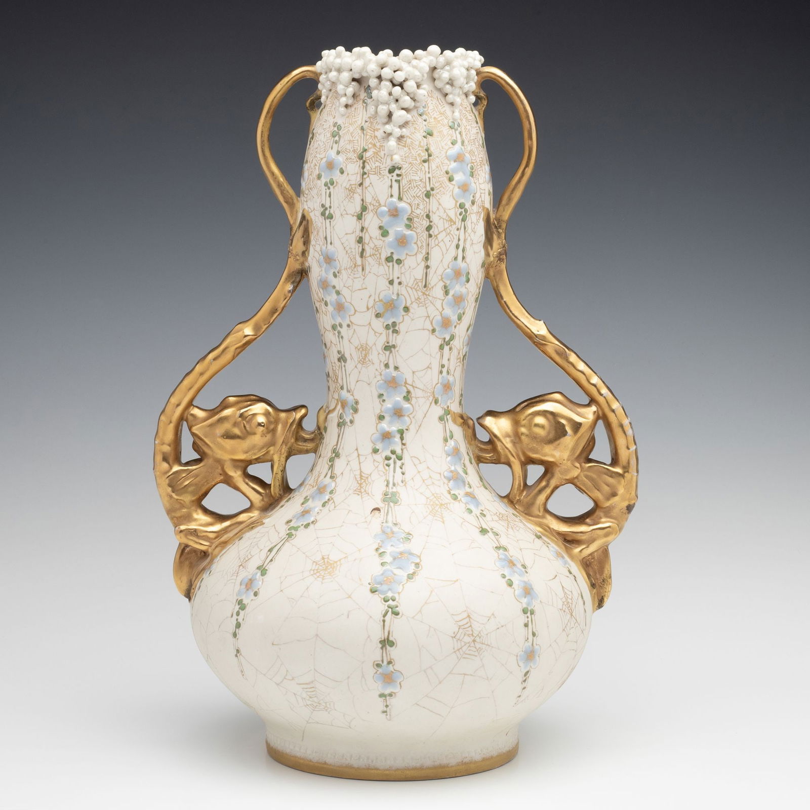 A 13-INCH AMPHORA VASE WITH GRIFFINS AND SPIDER WEBS: Early 20th Century The bulbous form with baluster neck is hand painted with gold tracery of spider webs joining vertical sprays of blue enamel forget-me-not flowers. Lavishly gilded handles formed as