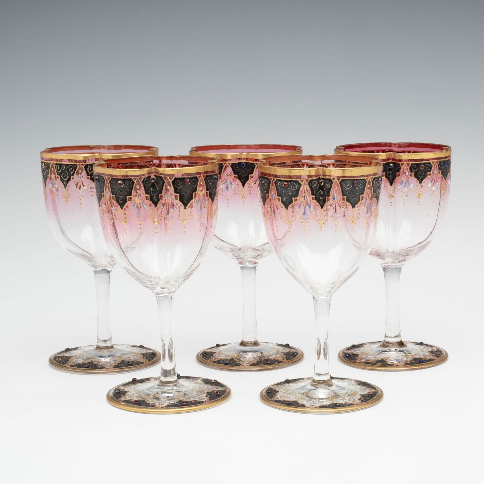 BOHEMIAN JEWELED & ENAMELED RUBINA ART GLASS WINES: Ludwig Moser Early 20th Century Each quatrefoil shape bowl is blown with four offset lobes and shaded ruby to clear, the top rim is embellished with black enamel pendants dressed in a colorful glass b