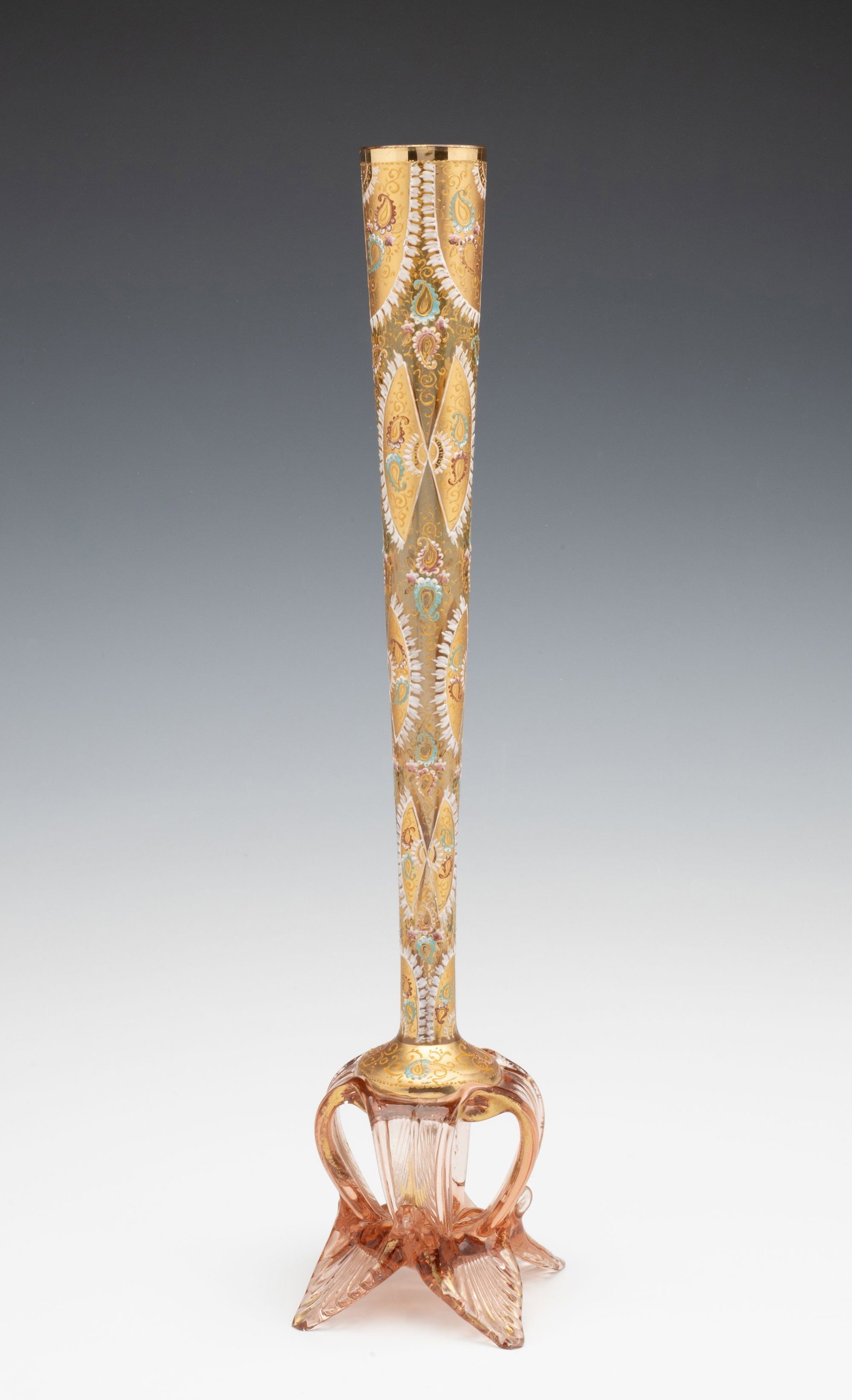A 17-INCH GILT AND ENAMEL BOHEMIAN ART GLASS VASE: Early 20th Century The tapering stick vase with paisley and fan motifs in relief enamels on gold is raised on an unusual pulled and tooled glass openwork base. Measures 17 x 4.75 with a 1.5 inch openi
