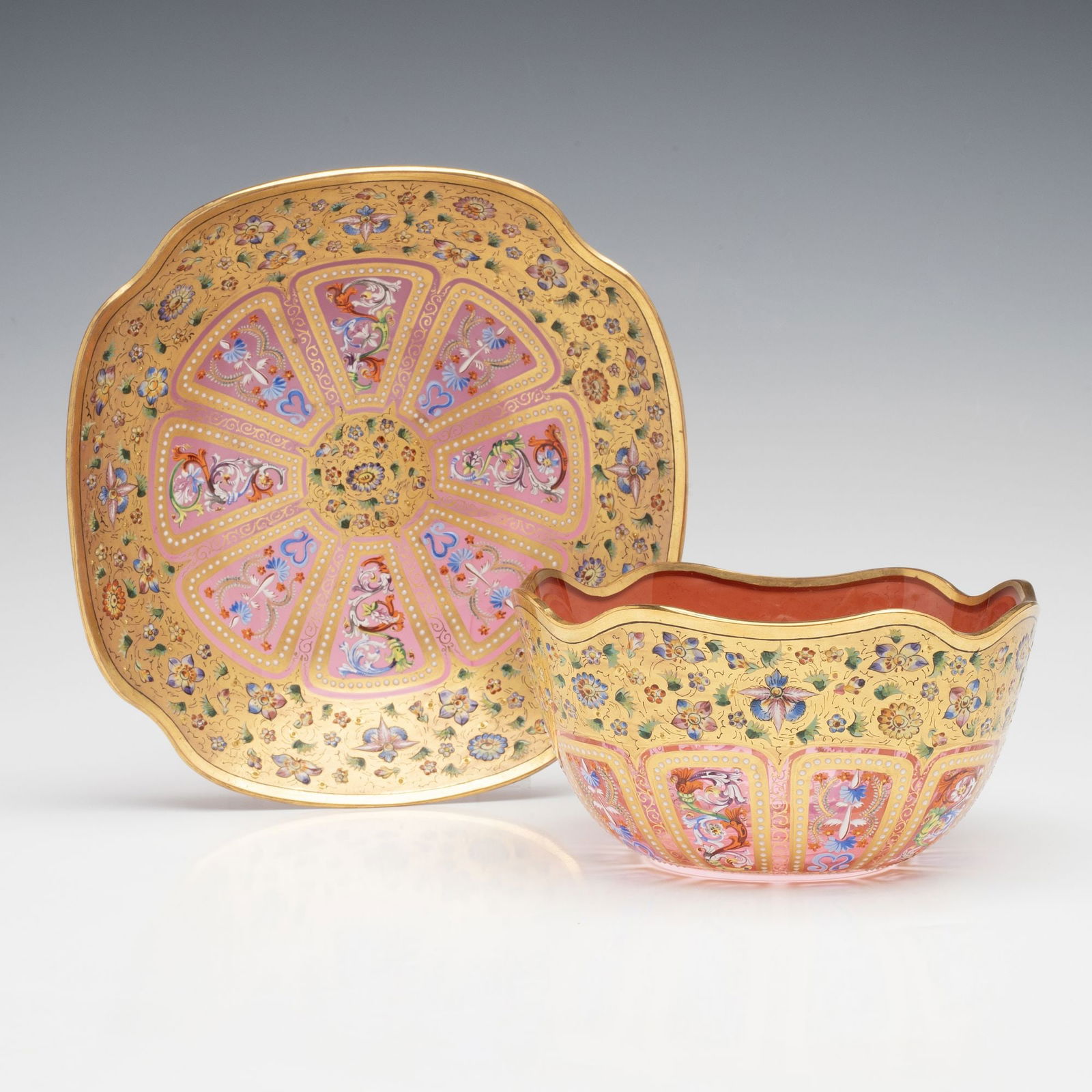 FINELY SHAPED AND DECORATED MOSER ART GLASS FINGER BOWL: Ludwig Moser Early 20th Century The jewel-toned cranberry glass finger bowl and underplate of shaped form are lavishly decorated in elegant gold covered in more than a dozen different colors of hand p