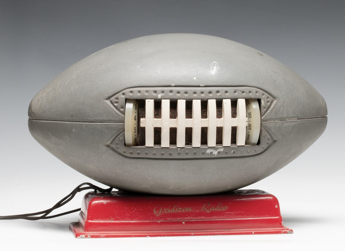 A 1940s FOOTBALL FORM RADIO BY EMPIRE RADIO, AMARILLO: The 'Gridiron Radio' by Empire Radio Company of Amarillo, Texas is cast from base metal in three pieces and painted grey with red enamel base. The 'football' houses an AM tuner with vertical knobs at 