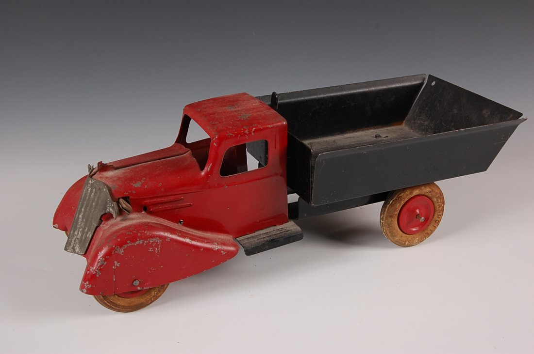 WYANDOTTE TOYS PRESSED STEEL DUMPTRUCK: Circa 1930s. With spring-loaded truck bed and white rubber tires. Measures 5.25 x 15 inches.