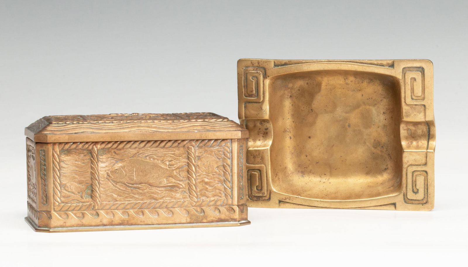 TIFFANY STUDIOS BRONZE CIGARETTE BOX AND ASH TRAY: The sarcophagus form box with hinged lid and aquatic motif with sailing ships numbered 1845 is accompanied by a Tiffany Studios 1133 Greek key ash tray. Measures 2 x 4.25 x 2.5 and the ashtray is 4.25