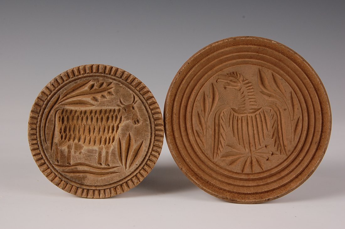 TWO TURNED WOOD BUTTER MOLDS, EAGLE & COW: Butter mold with a carved eagle crest clutching arrows and olive branches, measures 4.5 inches. Butter mold with primitive cow carving, measures 3.5 inches.