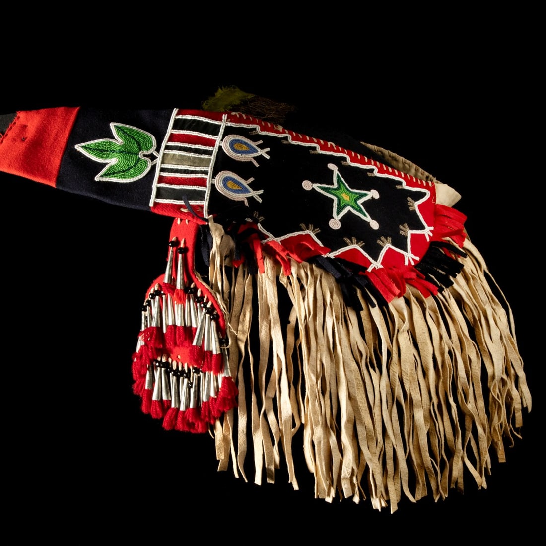 AN ELABORATE BEADED BLACKFEET HORSE CRUPPER CIRCA 1910: The Northern Plains horse crupper is constructed of wool cloth with native tanned leather, muslin, metal cones, yarn, glass beads, and cotton cloth. There are two roundels of large metal cones tipped