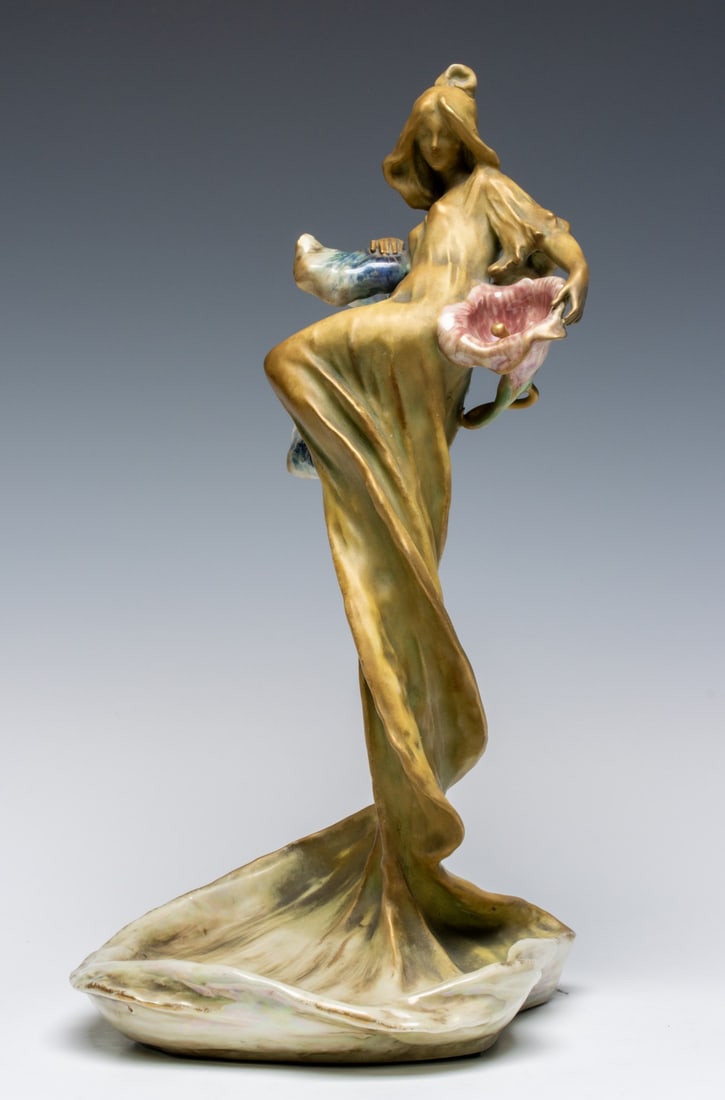 A REISSNER, STELLMACHER & KESSEL ART NOUVEAU FIGURE: Impressed Amphora on the base and marked with a red Riessner, Stellmacher & Kessel ink stamp, the figure in matte green and gold holding high glaze blossoms and leaves in blue and red. Measures 15