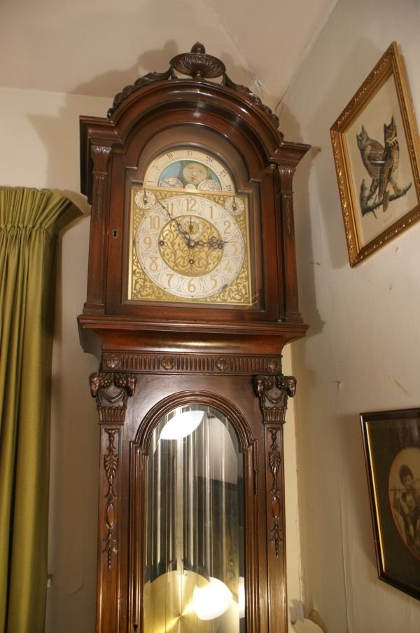 ADAM STYLE 7 TUBE CARVED WALNUT GRANDFATHER CLOCK: Made by Colonial Mfg and marked on the dial and works. Slide off hood with a top urn pediment, ram's heads at the corners, arched beveled glass, applied carvings and bun feet. Brass dial with silvered