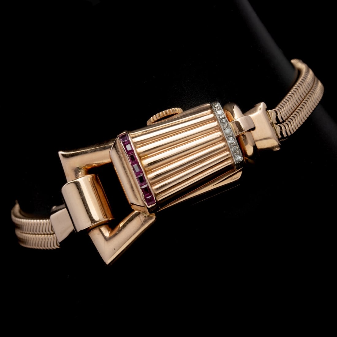 A LADIES ART MODERNE 14K ROSE GOLD WATCH WITH GEMSTONES: The Art Moderne 14K gold ladies hidden wristwatch with sculptural fluted case is accented with channel-set rubies and diamond trim, mounted on a double snake-chain bracelet. Stamped 14k on the case an