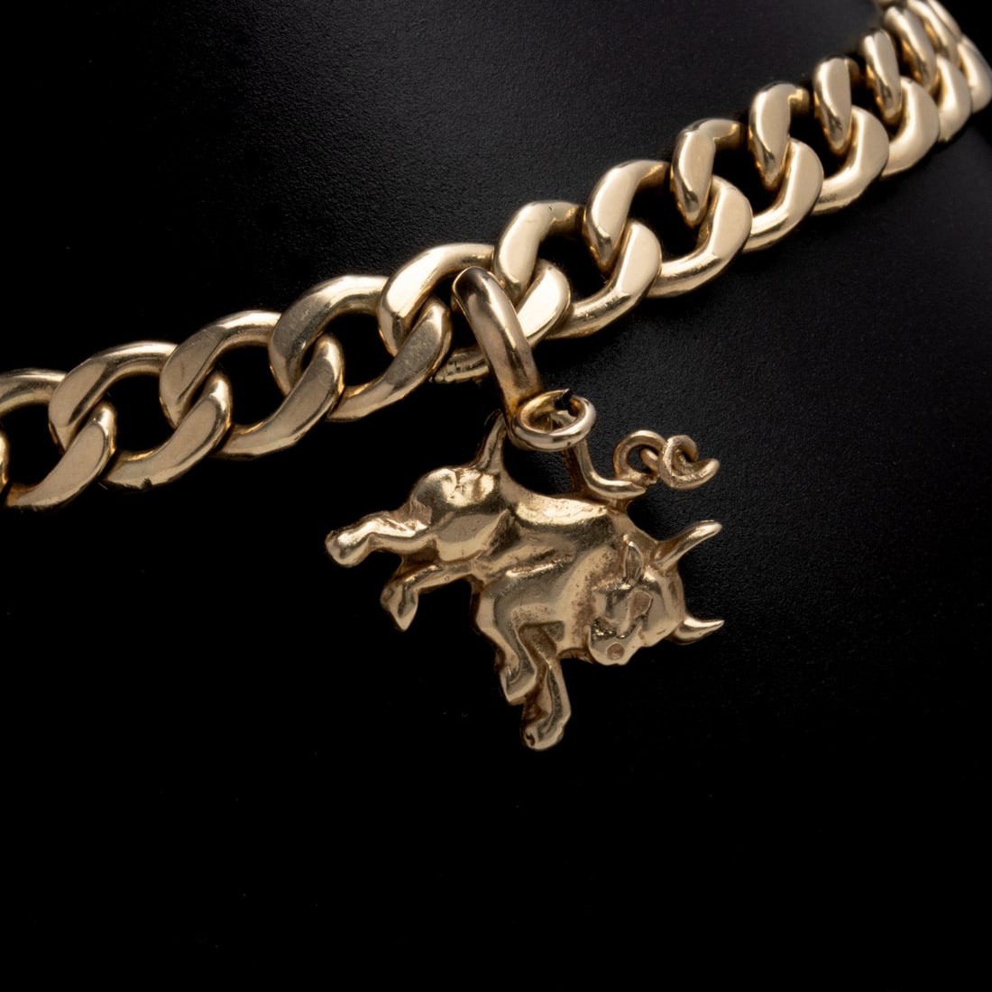 A HIGH QUALITY 14K GOLD CURB LINK CHARM BRACELET: The heavy curb link charm bracelet composed of wide flattened links is stamped 14k on the clasp and suspends a figural bull charm also marked 14k. Bracelet length is 8.25 inches. Charm is 0.5 x 0.5 in