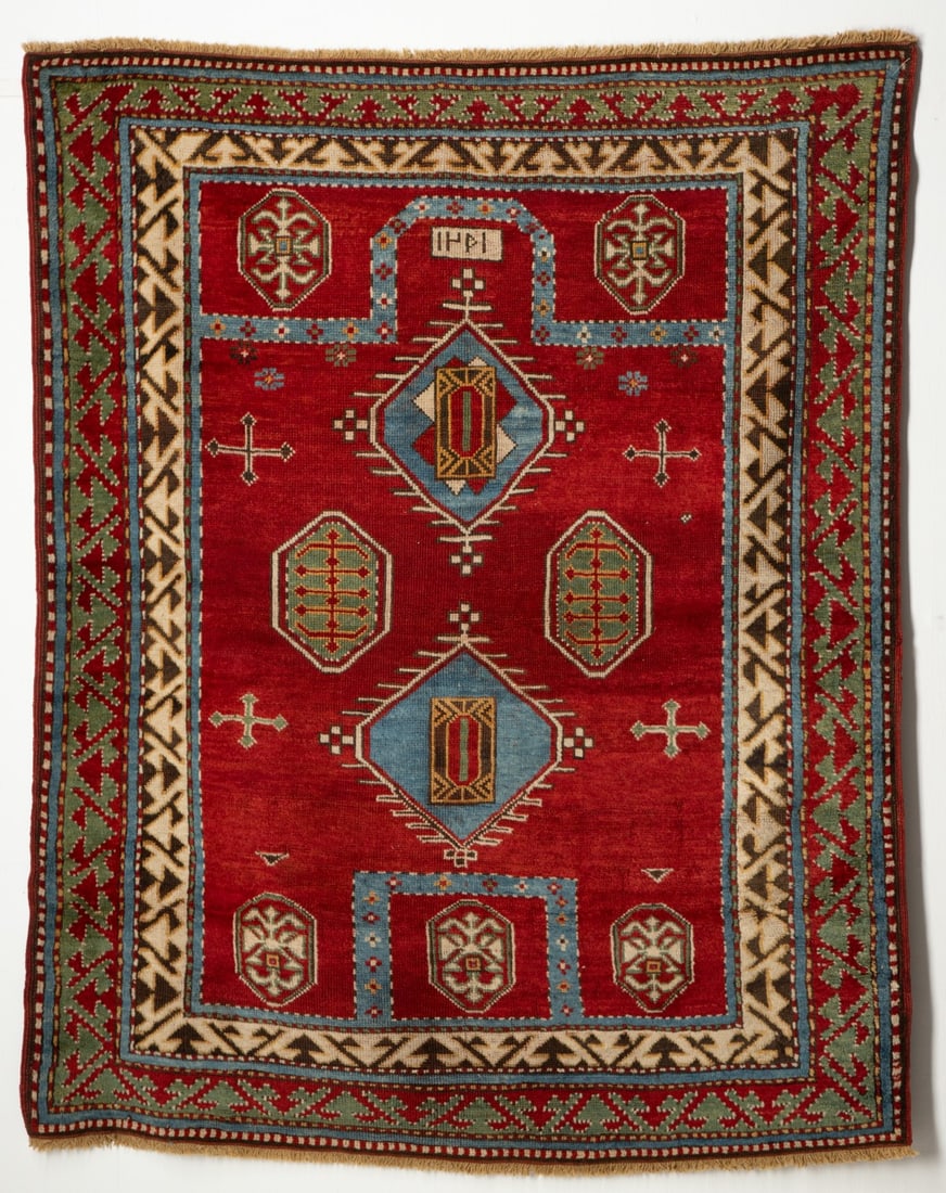 A BORDJALU KAZAK PRAYER RUG, DATED AH 1251/ AD 1835: The abrashed red field with two pale blue hexagonal medallions supported by two green hexagonal medallions and four cruciform motifs below a pale blue arch enclosing a date inscription, within two rec