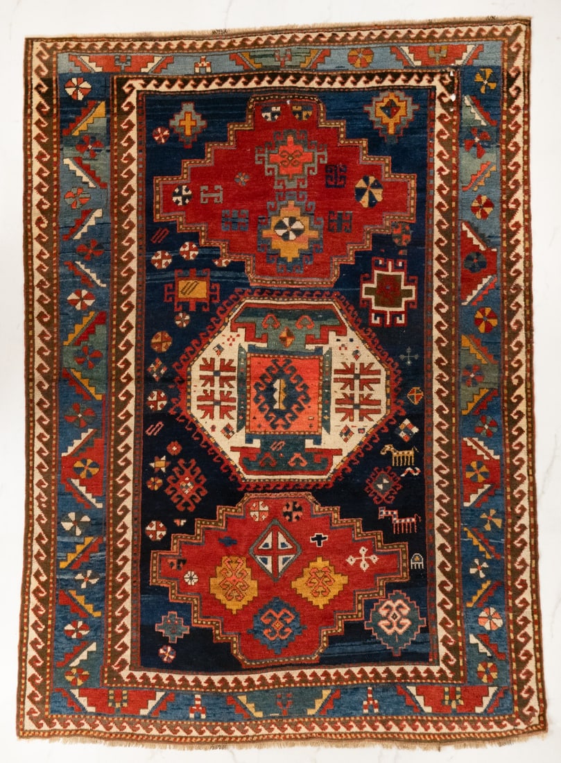 A KAZAK KARACHOV RUG, WEST CAUCASUS, CIRCA 1900: The blue field with a central ivory octagonal hooked medallion between two stepped chestnut medallions enclosing scattered flora forms, supported by scattered flora and two ibex, within an ivory recip