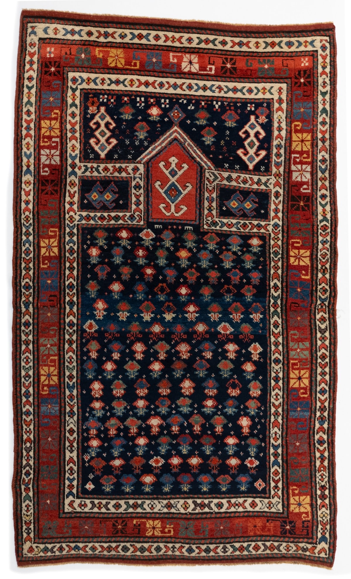 A FINE UNUSUAL KAZAK PRAYER RUG, LATE 19TH CENTURY: The blue field with overall offset rows of flowering plants below a pointed arch with a plant filled red reserve flanked by ivory framed blue rectangular panels below blue plant spandrels, within a re