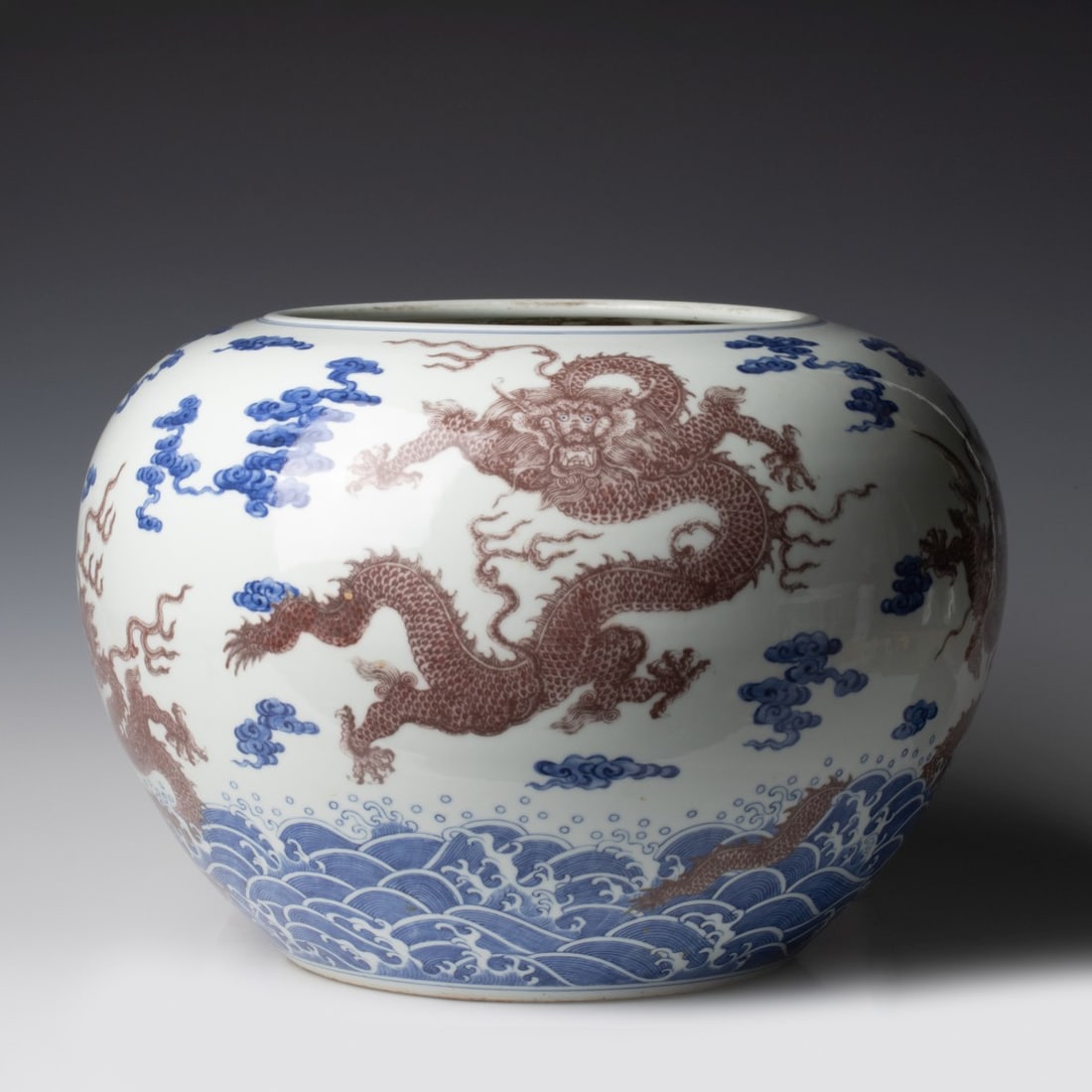 A FINE LARGE 19C. CHINESE DRAGON-DECORATED FISH BOWL: The Qing dynasty porcelain fish bowl is heavily potted with deep rounded sides rising to a lipped rim, the exterior vividly decorated in iron-red with five animated five-clawed dragons in pursuit amid