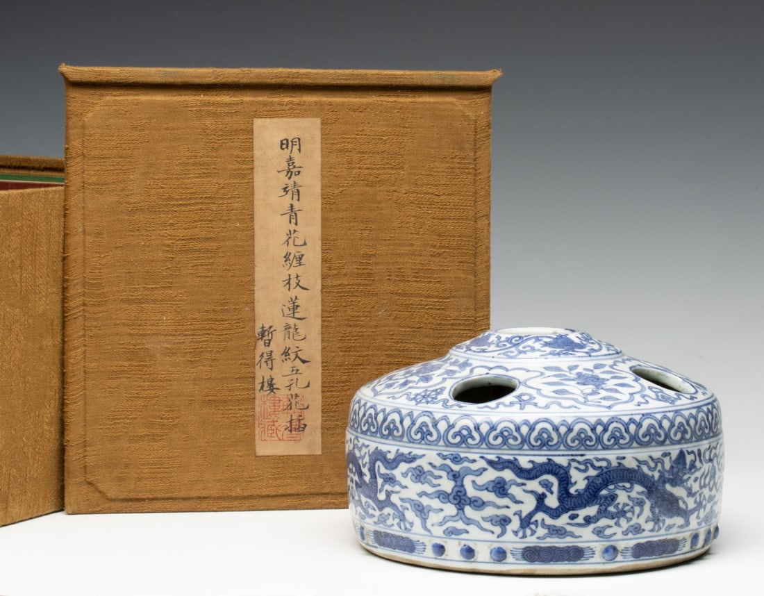 AN ANTIQUE JAPANESE BLUE AND WHITE PORCELAIN IKEBANA: The porcelain basin form multi-hole ikebana or flower arranger in cloth-covered box is decorated with undulating dragons amid traditional motifs in blue on white. Measures 4.75 x 8.25 inches in