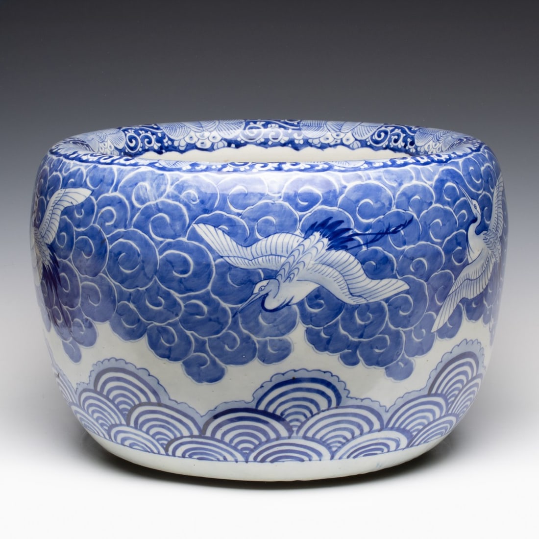 AN EARLY 20TH C. JAPANESE BLUE & WHITE HIBACHI W/CRANES: The large hand painted blue and white porcelain hibachi is decorated with flying cranes against cloud motif in cobalt on white above ocean waves (Seigaiha) also in hand painted cobalt. Measures