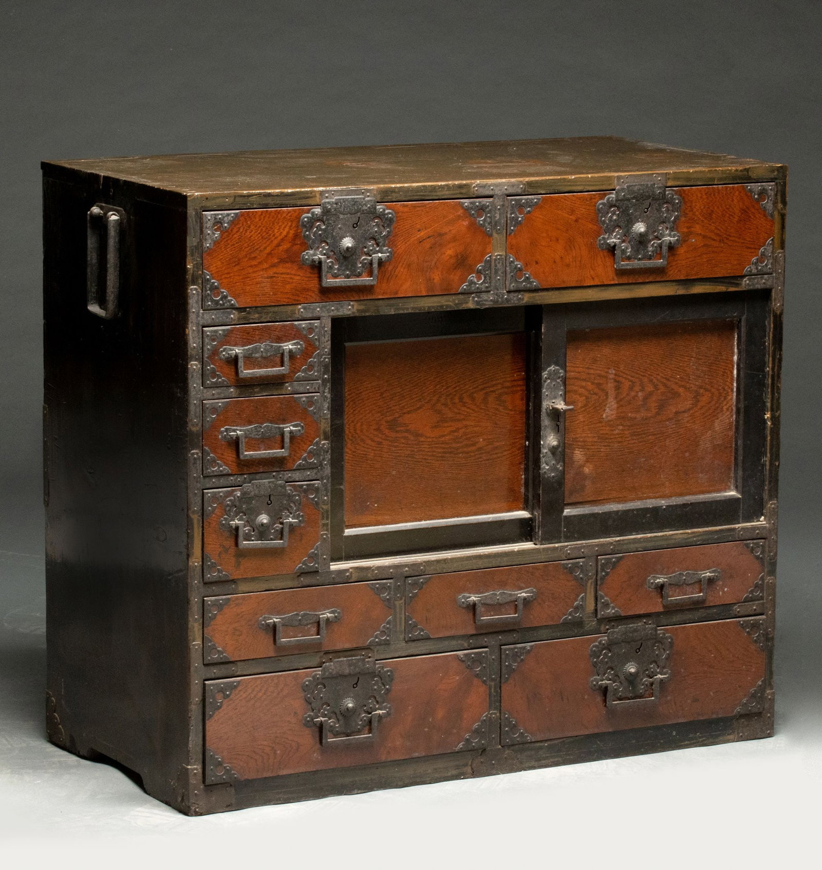 A GOOD KEYAKI WOOD AND EBONIZED JAPANESE CHEST: The iron mounted chest with drawers and sliding doors on the right is fronted by keyaki wood displaying finely figured grain behind the riveted and oxidized iron. Measures 31 x 35 x 17.25 inches. 