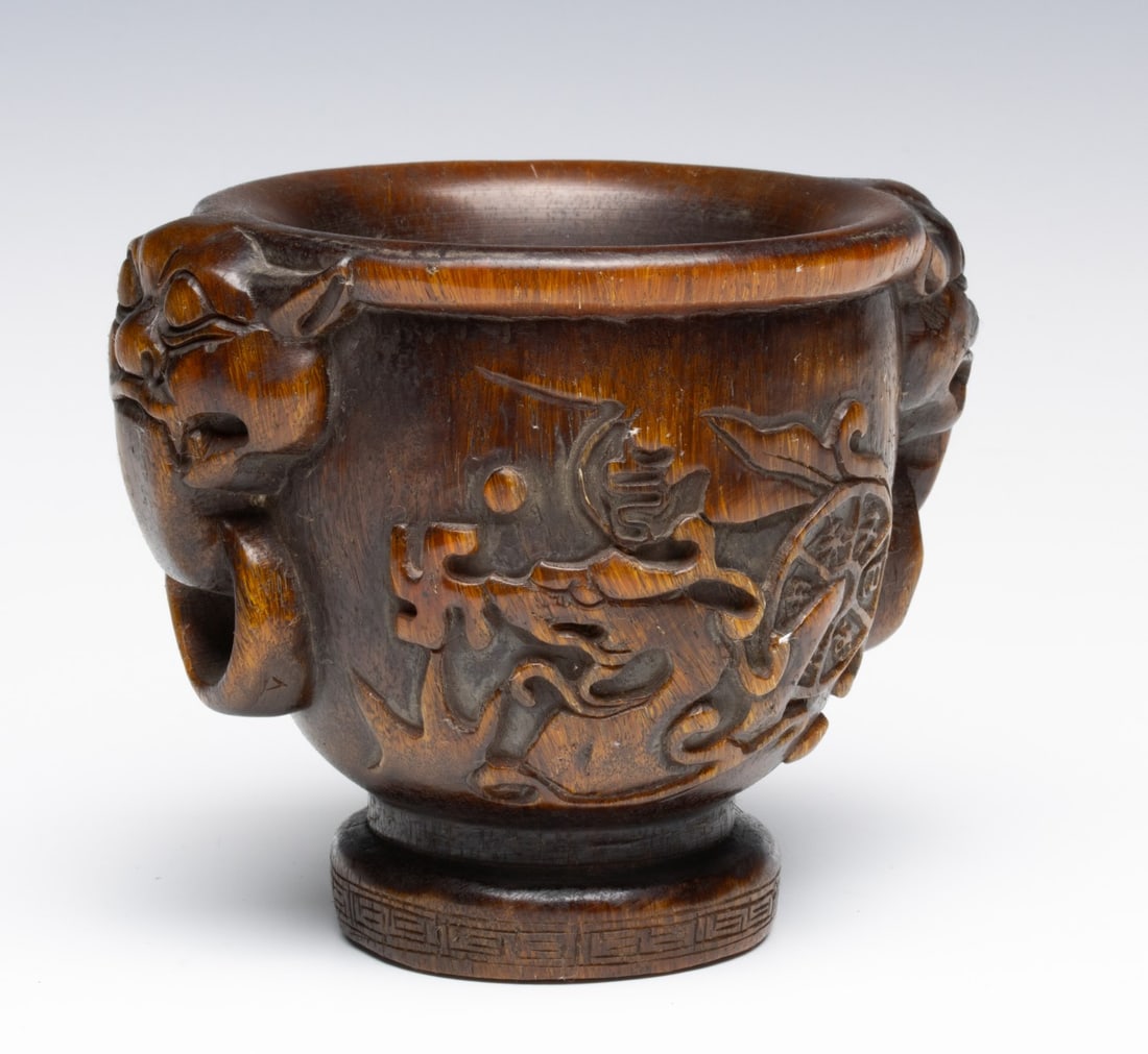 A CHINESE CARVED WATER BUFFALO HORN LIBATION CUP: The footed cup or vessel carved with elephant heads each end, a workshop mark carved on the base. Measures 4.5 x 6 x 4.5 inches. Provenance: The estate of John Adair Jr. (1942-2025), founder and