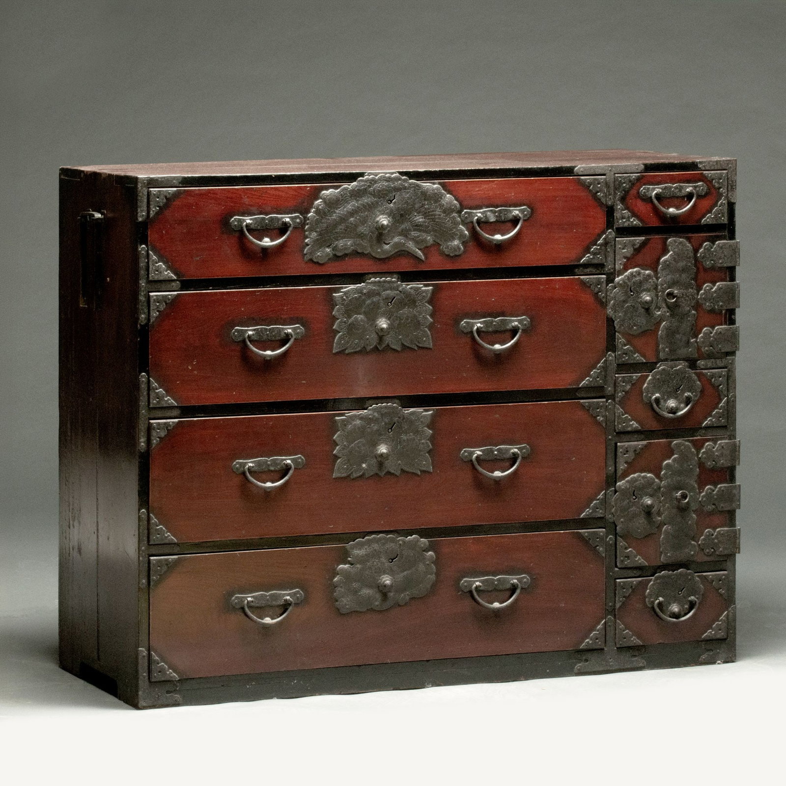 AN ELABORATE 19TH C. JAPANESE TANSU WITH SCULPTED IRON: The case of drawers and doors with handles each end is warmly patinated, as are the elaborate iron mounts cut with floral motifs, the uppermost metal plate worked in the image of a ho-ho or phoenix bi