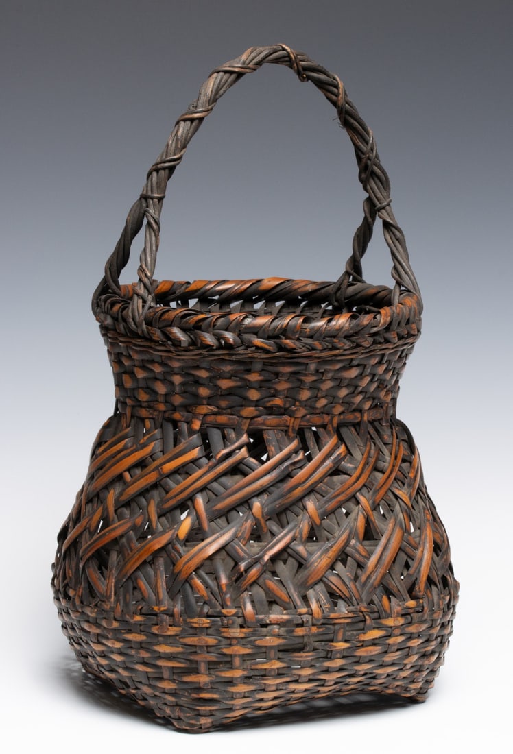 A TIERED JAPANESE BAMBOO IKEBANA BASKET, ADAIR ESTATE: The basket of three-tiered weaving construction has a tight twill weave transitioning into a central band of broad-splint diagonal openwork capped by a dense, textured neck. The wide, rolled rim is he