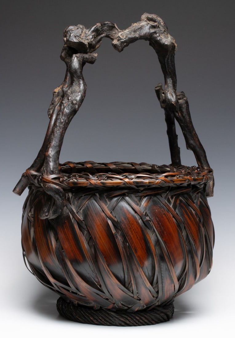 JAPANESE BAMBOO AND ROOT IKEBANA BASKET, ADAIR ESTATE: The handsome example of globular form is woven with interlocking bamboo splints that create a dynamic, swirling motion around the vessel like waves. The dramatic handle of gnarled, primeval stalks joi