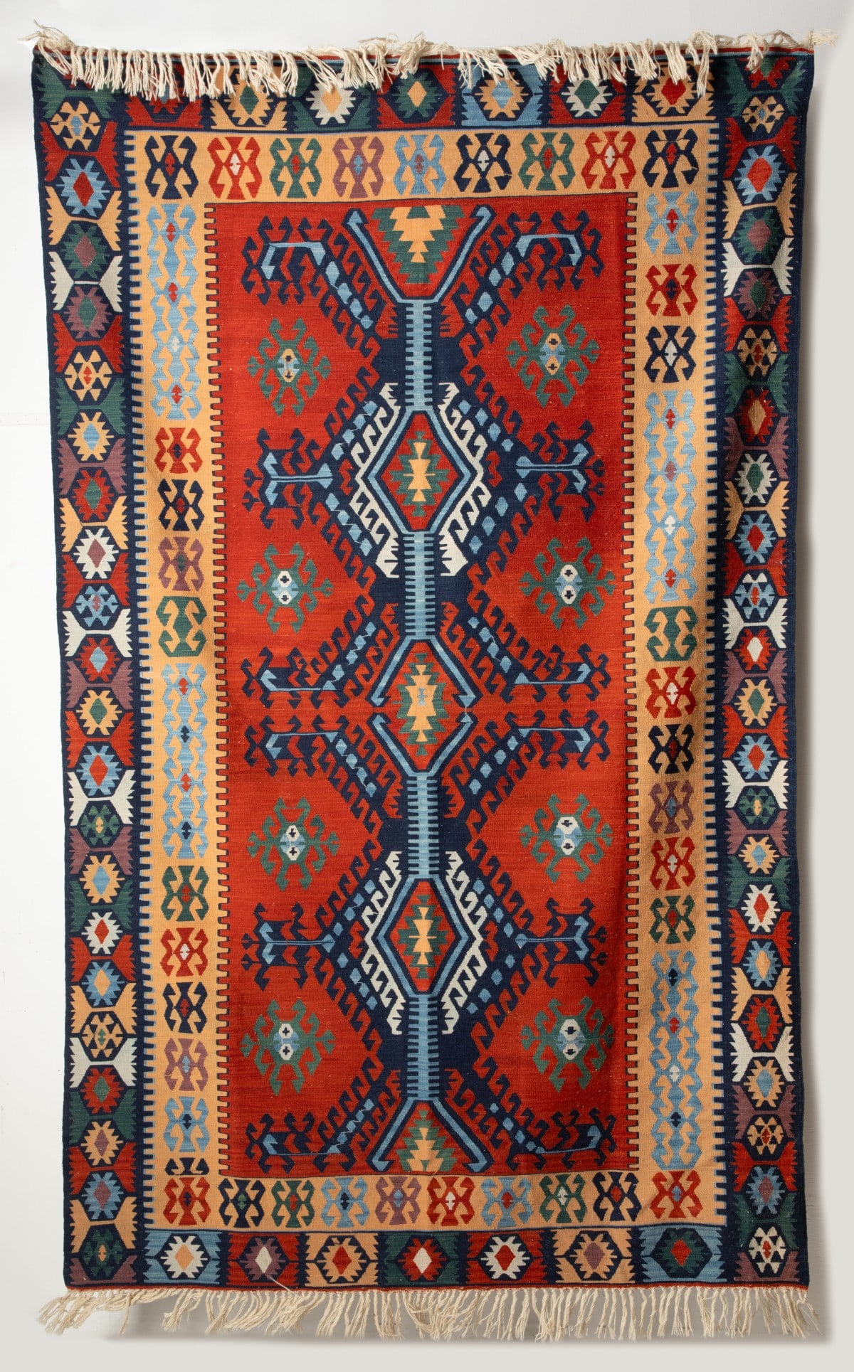 A MODERN TURKISH KILIM, CENTRAL TURKIYE: the terracotta field with a column of three conjoined layered hooked rhombus medallions supported by two columns of four green medallions, within an inner cream surround enclosing hooked medallions,