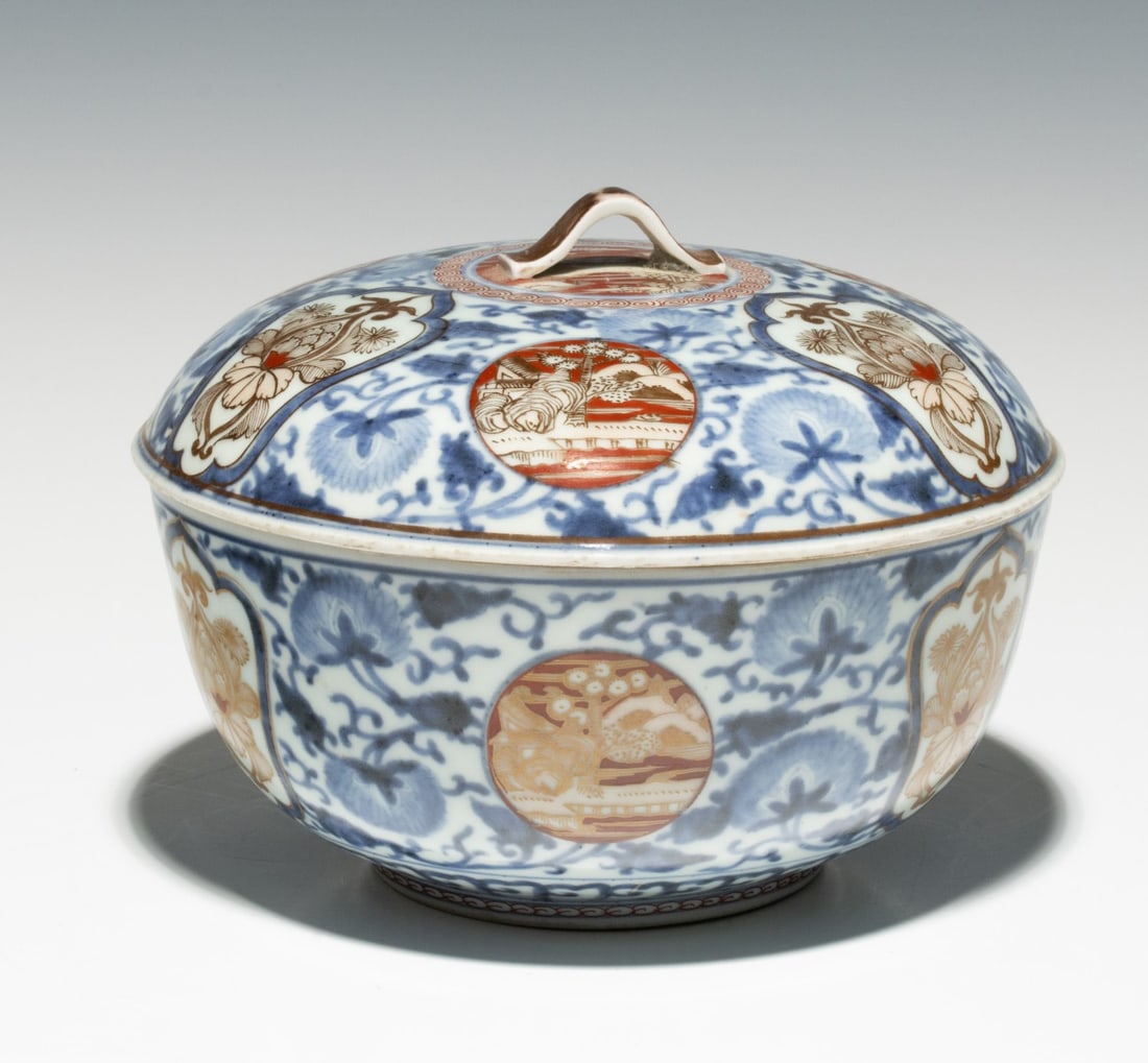 A MEIJI PERIOD ARITA KILN PORCELAIN IMARI BOWL: The unmarked lidded bowl is decorated in circular windows and cartouches with red and gold against an underglaze blue and white ground. Measures 5.75 x 8 inches in diameter. Provenance: The estate