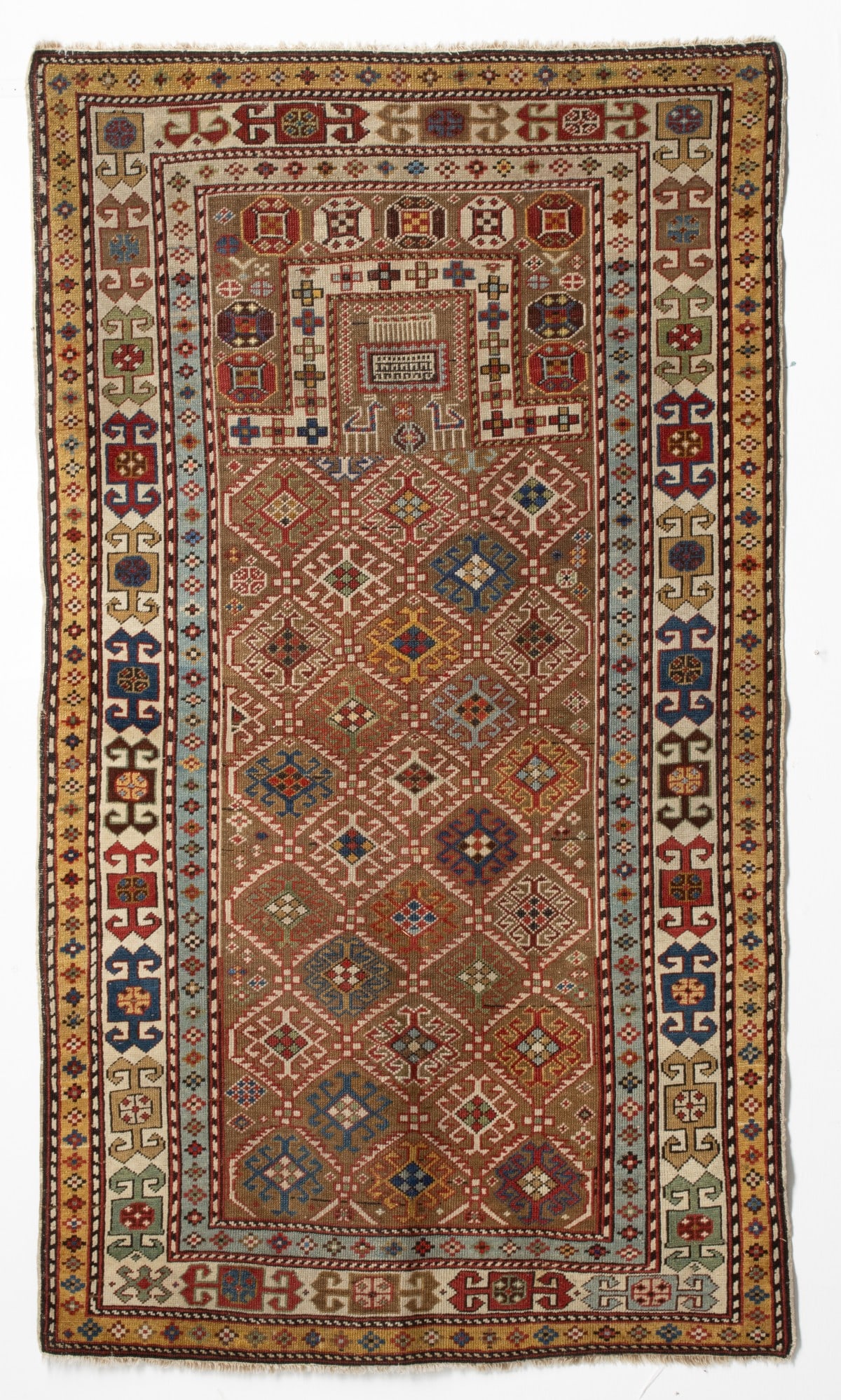 UNUSUAL AKSTAFA PRAYER RUG, CIRCA 1900: the caramel mihrab with a serrated leaf lattice enclosing offset rows of pastel polychrome hooked lozenge medallions below a flattened arch enclosing a pair of ibex and comb dais, caramel spandrels