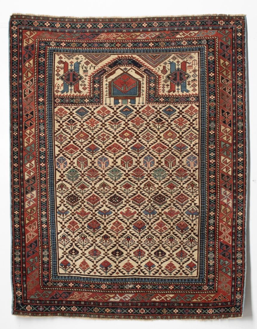 DAGHESTAN PRAYER RUG, NE CAUCASUS, CIRCA 1880: The ivory mihrab with an allover linked serrated leaf lattice enclosing offset rows of multifarious flowering plants below a flattened chamfered arch, ivory spandrels enclosing mirrored lozenge medall