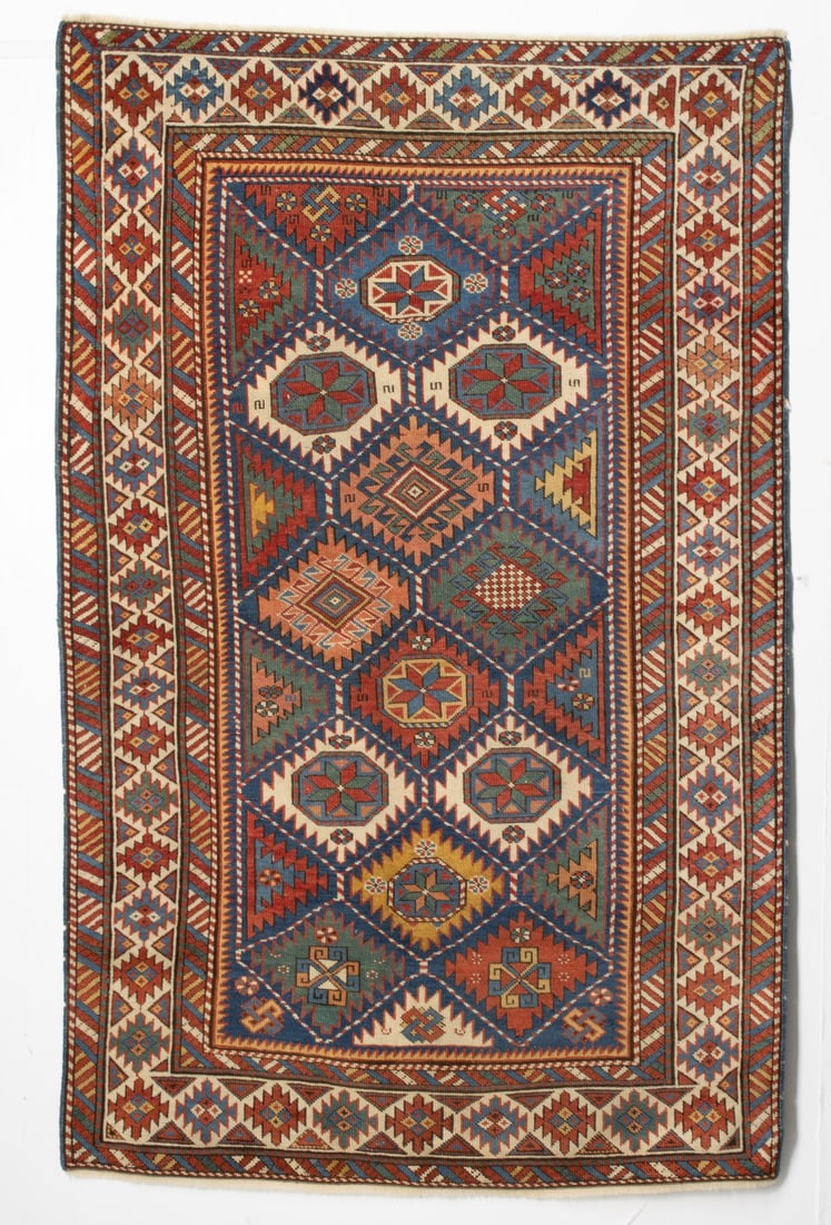 KUBA RUG, NE CAUCASUS, LAST QUARTER 19TH CENTURY: The blue field with a rhombus lattice enclosing alternating octagonal polychrome guls and hooked diamonds within an ivory continuous serrated medallion border, diagonal polychrome banded guard