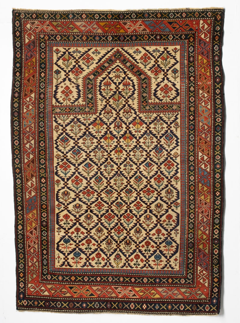 DAGHESTAN PRAYER RUG, DATED AH 1220/AD 1805: The ivory mihrab with a serrated leaf lattice enclosing offset rows of multifarious flowering plants, with a pointed arch, similar ivory plant spandrels, within a red diagonal hooked block border. Mea