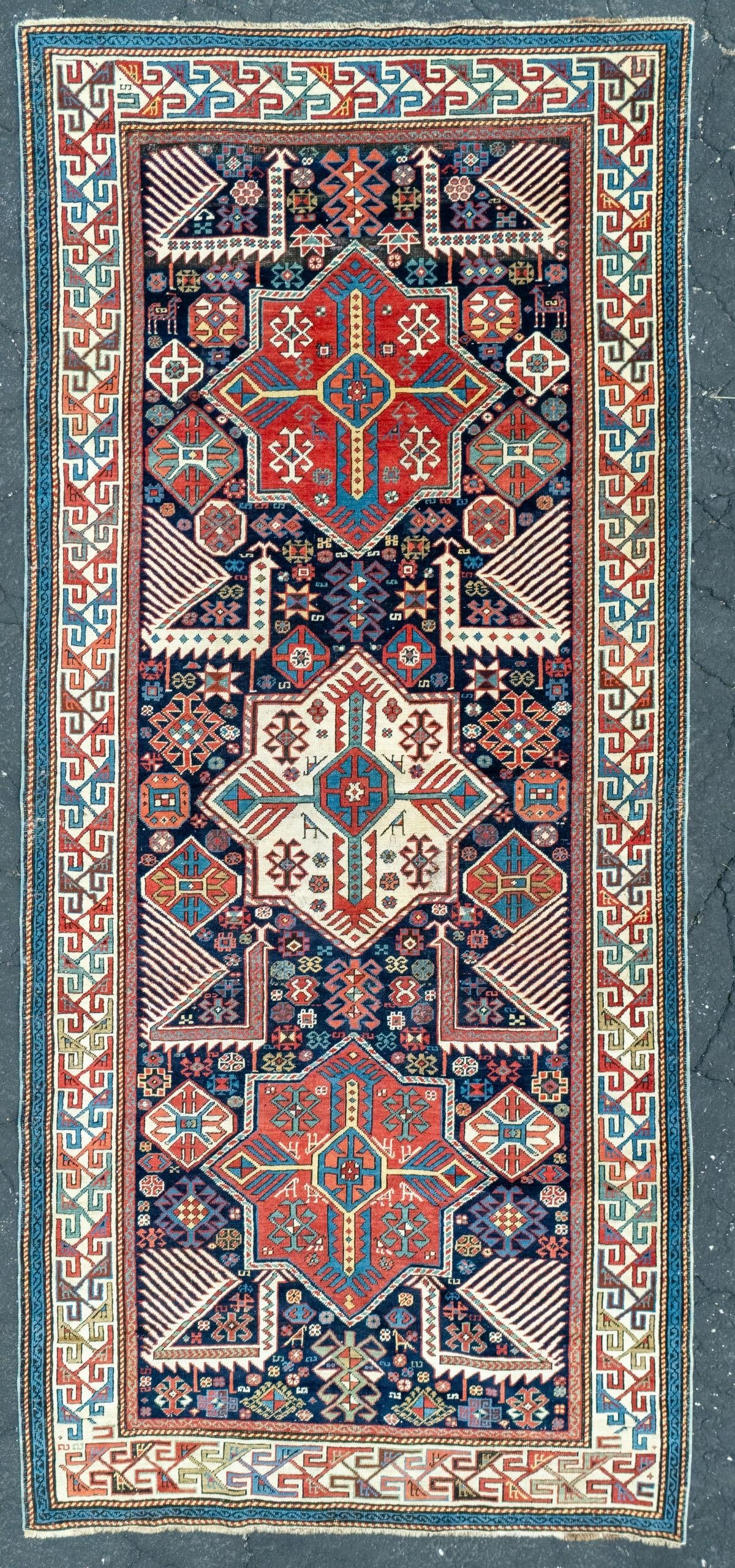FINE AKSTAFA RUG, EAST CAUCASUS, circa 1875: The blue field with a central ivory star medallion between two similar red medallions, flanked on either side by open tail peacocks, supported by scattered flora forms and a pair of small ibex, within