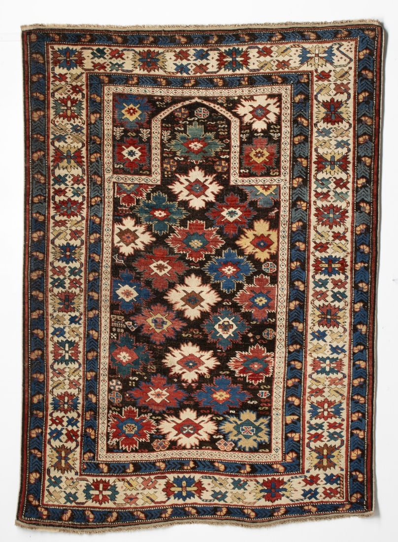 SHIRVAN 'BLOSSOM' PRAYER RUG, EAST CAUCASUS, C 1875: The charcoal mihrab with overall offset rows of blazen flower heads supported by scattered small flora, below a rounded arch, blazen flower head spandrels, within an ivory serrated flower head, bracke