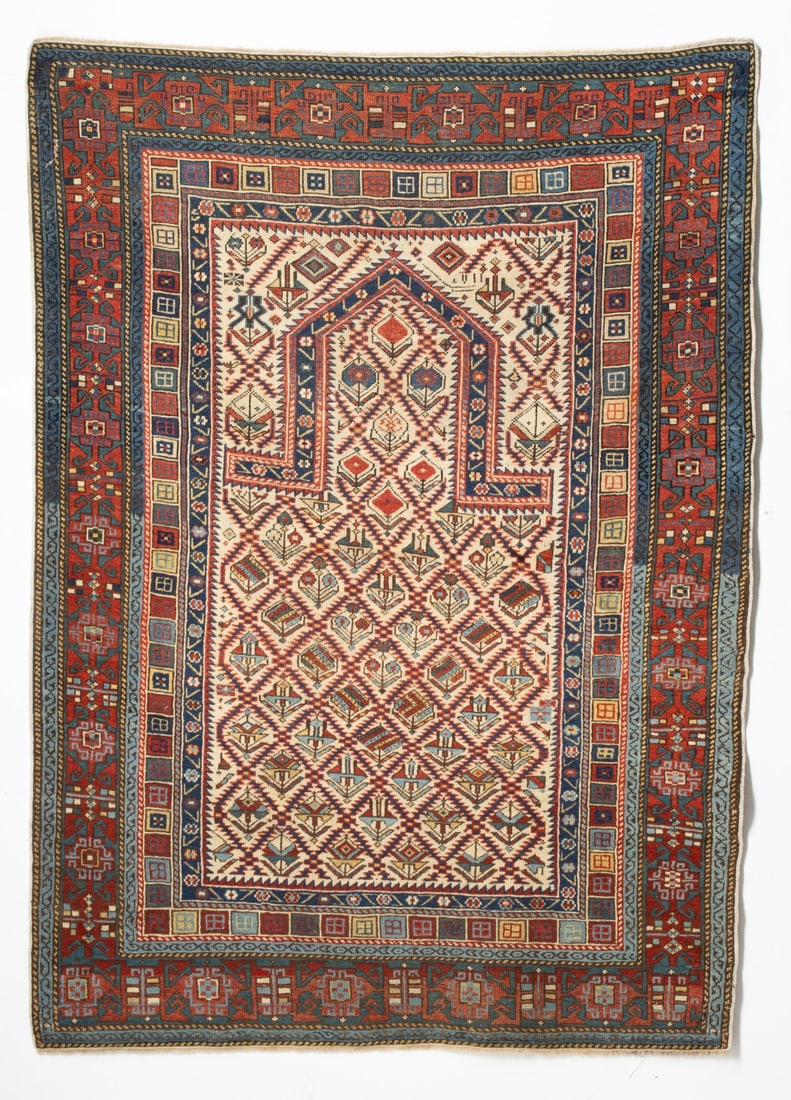 FINE RARE SHIRVAN PRAYER RUG, EAST CAUCASUS, C. 1880: The ivory mihrab with an allover serrated leaf lattice enclosing multifarious polychrome flowering plants, within a chamfered pointed arch, similar ivory plant lattice spandrels within an inner polych