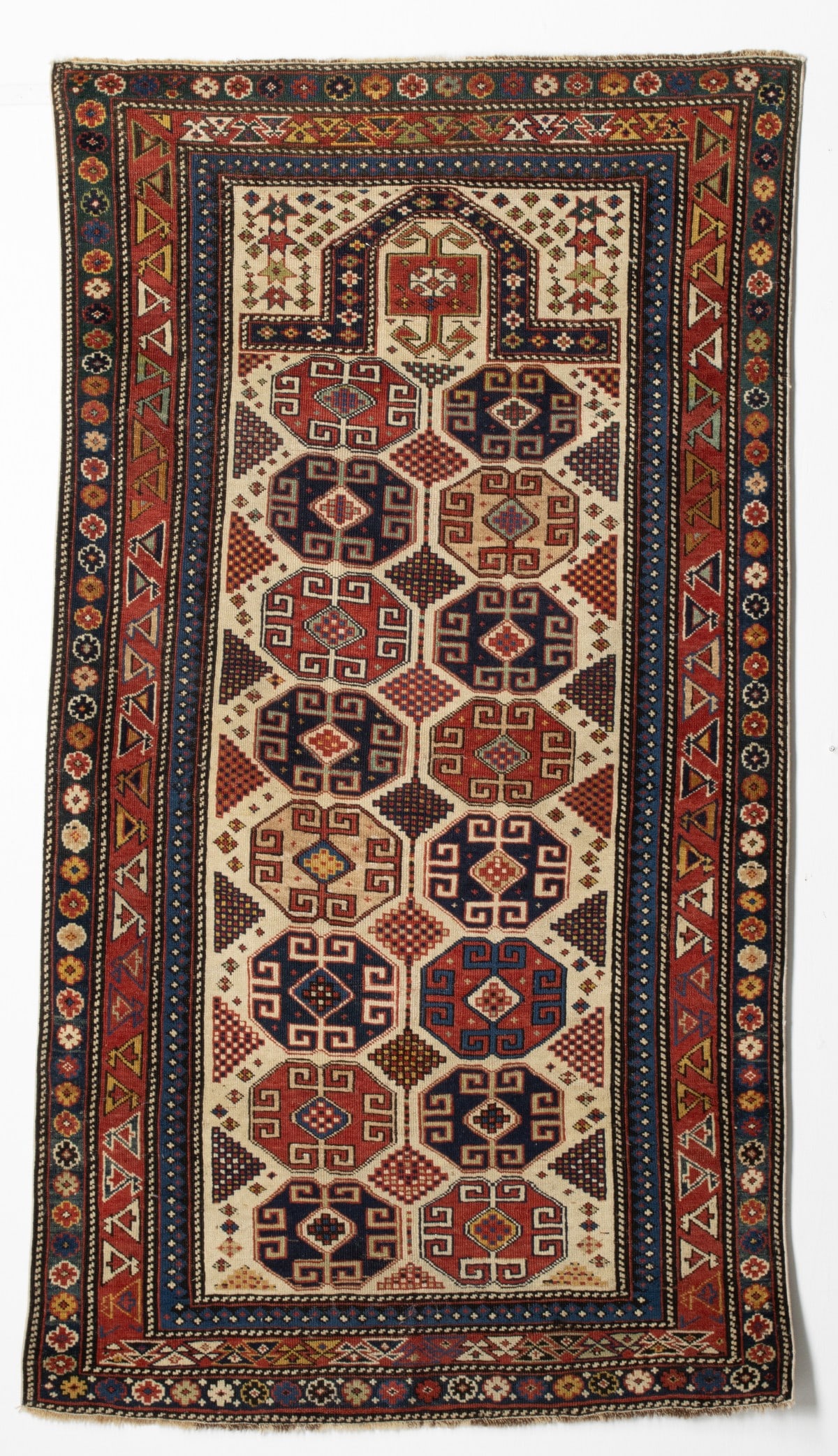 FINE RARE MOGHAN PRAYER RUG, CIRCA 1870: The ivory mihrab with two columns of eight hooked octagonal medallions around a column of conjoined polychrome rhombus medallions within similar outer half medallions below a konchanak gul within a ch
