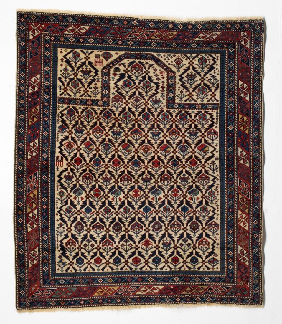 FINE SHIRVAN PRAYER RUG, EAST CAUCASUS, CIRCA 1880: The ivory mihrab with an allover stepped leaf lattice enclosing offset rows of multifarious plants, a singe ibex and two differing flowering plants, below a champfered flattened arch, ivory plant latt