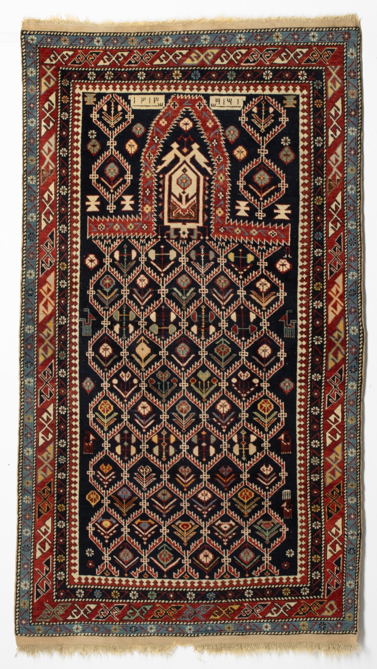 KARAGASHLI PRAYER RUG, DATED AH 1313/AD 1895: The dark blue mihrab with an allover serrated leaf lattice enclosing offset rows of multifarious flowering plants supported by small animals below a pentagonal medallion within an elongated serrated r