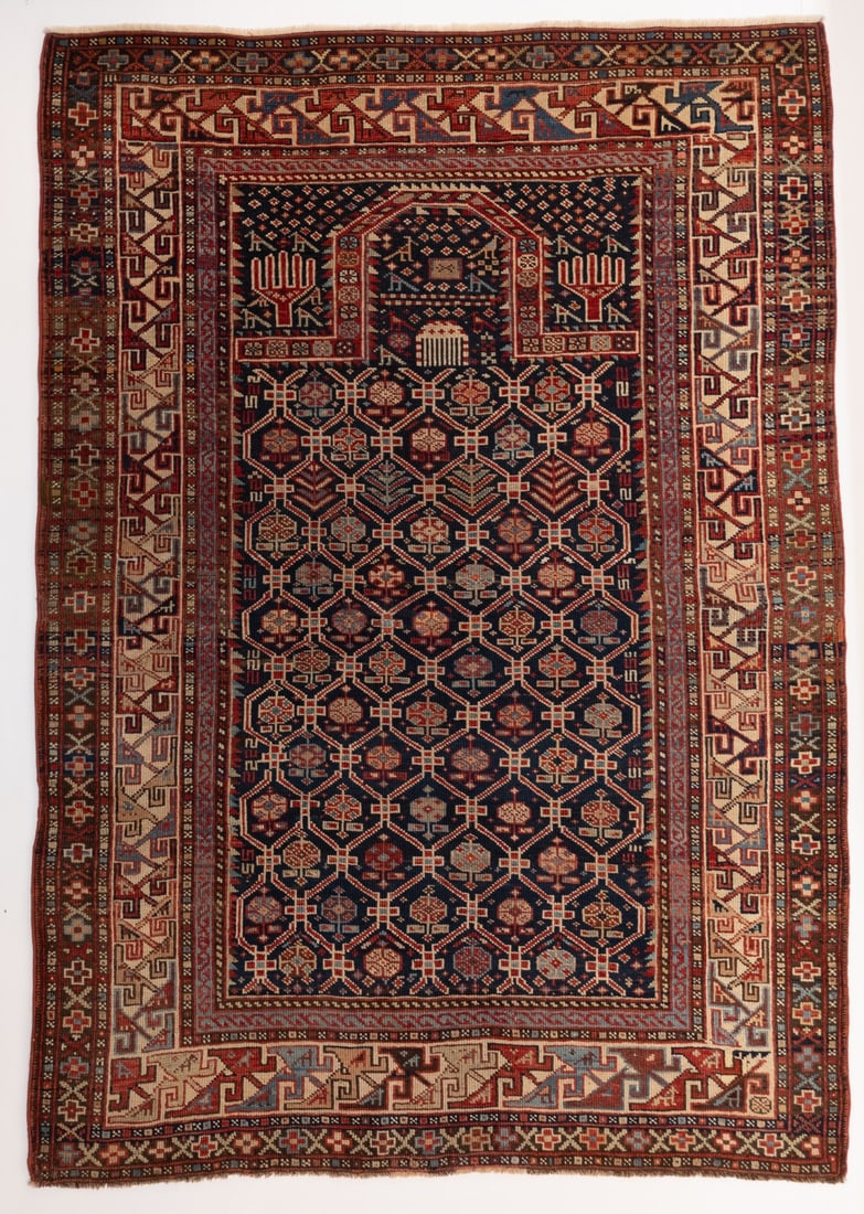 SHIRVAN PRAYER RUG, EAST CAUCASUS, LATE 19TH C: The blue mihrab with offset rows of flowering plants within a rhombus lattice linked by cruciform medallions, below a comb dais, small flower heads and a pair of small birds within a flattened arch, h