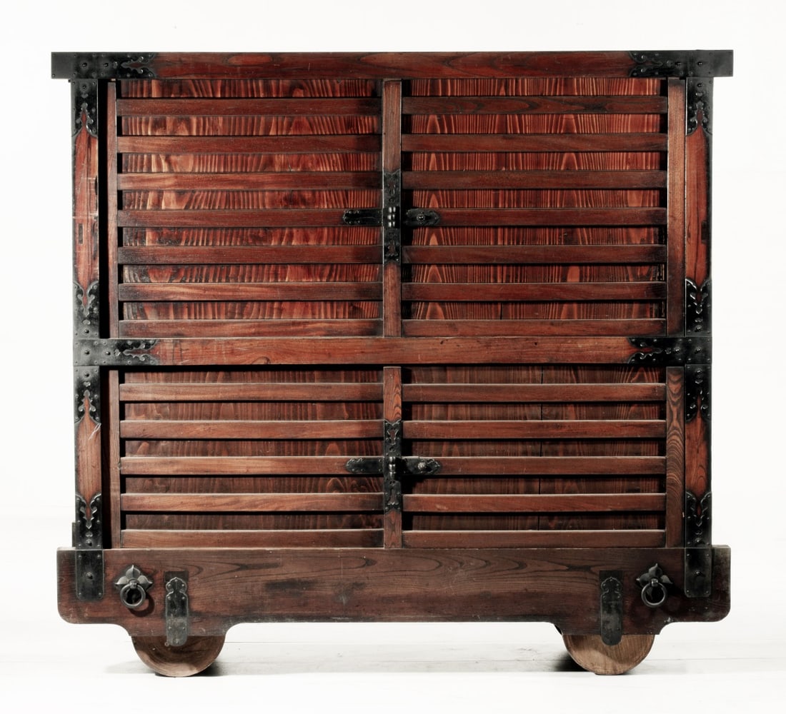 A MONUMENTAL 19TH CENTURY JAPANESE 60-INCH KURUMA DANSU: The massive chest on wheels with slatted doors and cabinet ends is of mortise and tenon construction with keyaki wood framing and iron strapwork. The doors open to an paulownia wood interior with shel