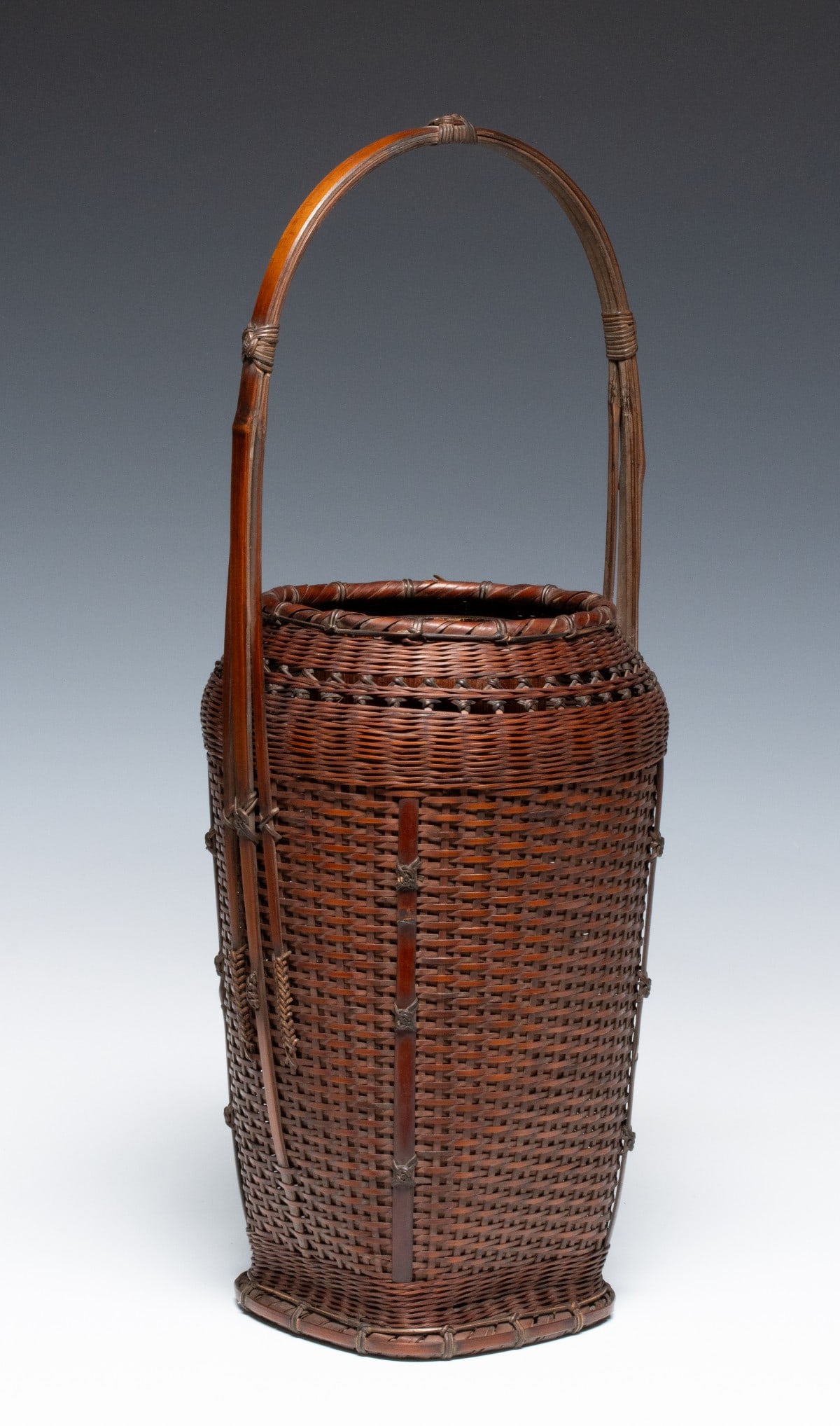 A JAPANESE BASKET SIGNED CHIKUYOSAI, ADAIR ESTATE: The tall, slender vessel is constructed with a dense plain-weave body spaced by vertical bamboo stays, each secured with intricate decorative knotting in black bamboo below an open-work band laced in 