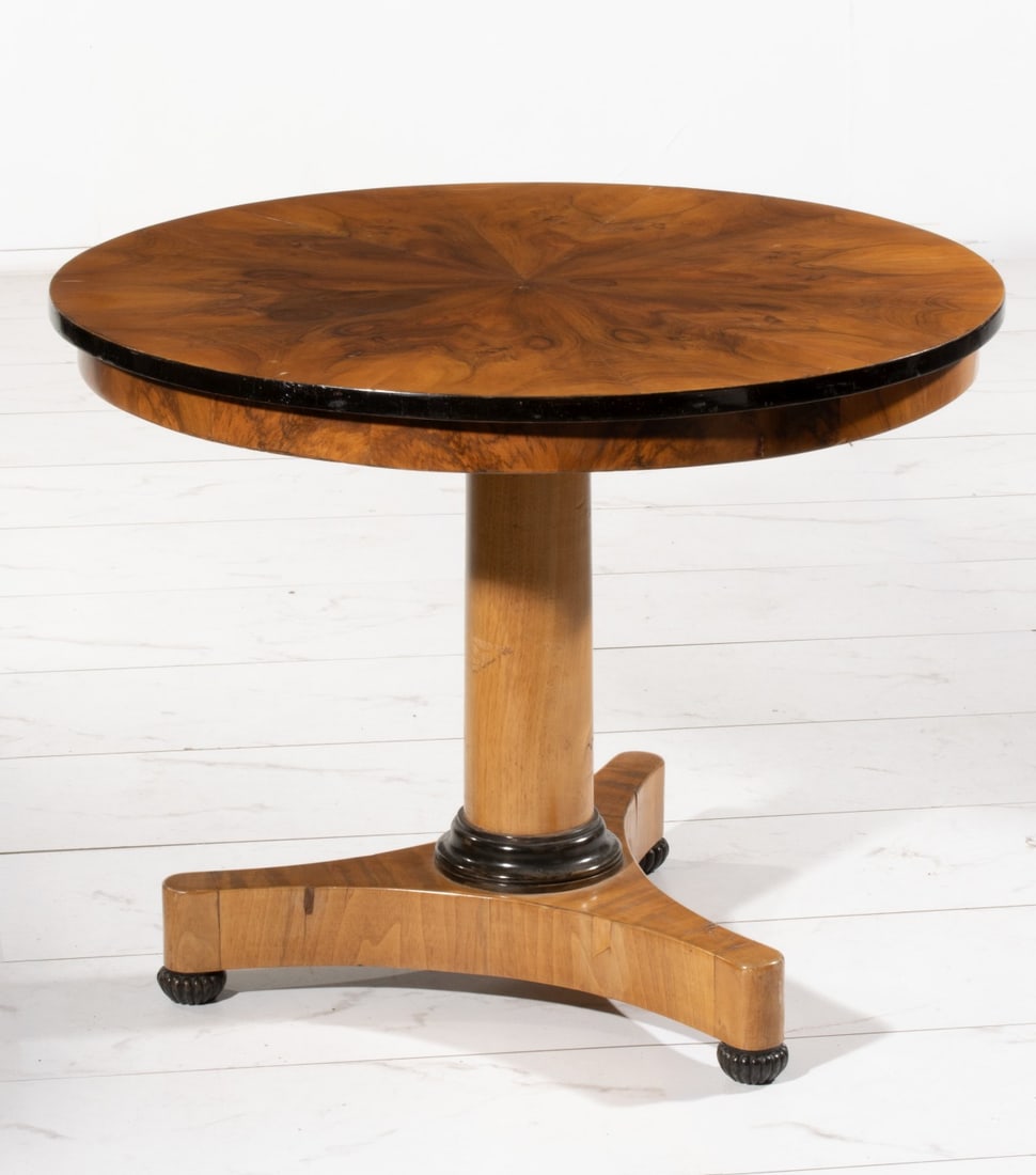 A SMALL LATE 19TH CENTURY BIEDERMEIER CENTER TABLE: The classic Biedermeier fruitwood center table of smaller scale is accented in bookmatch veneers and ebonized details. Measures 27 x 34 inches in diameter. Provenance: The estate of John Adair Jr. (19