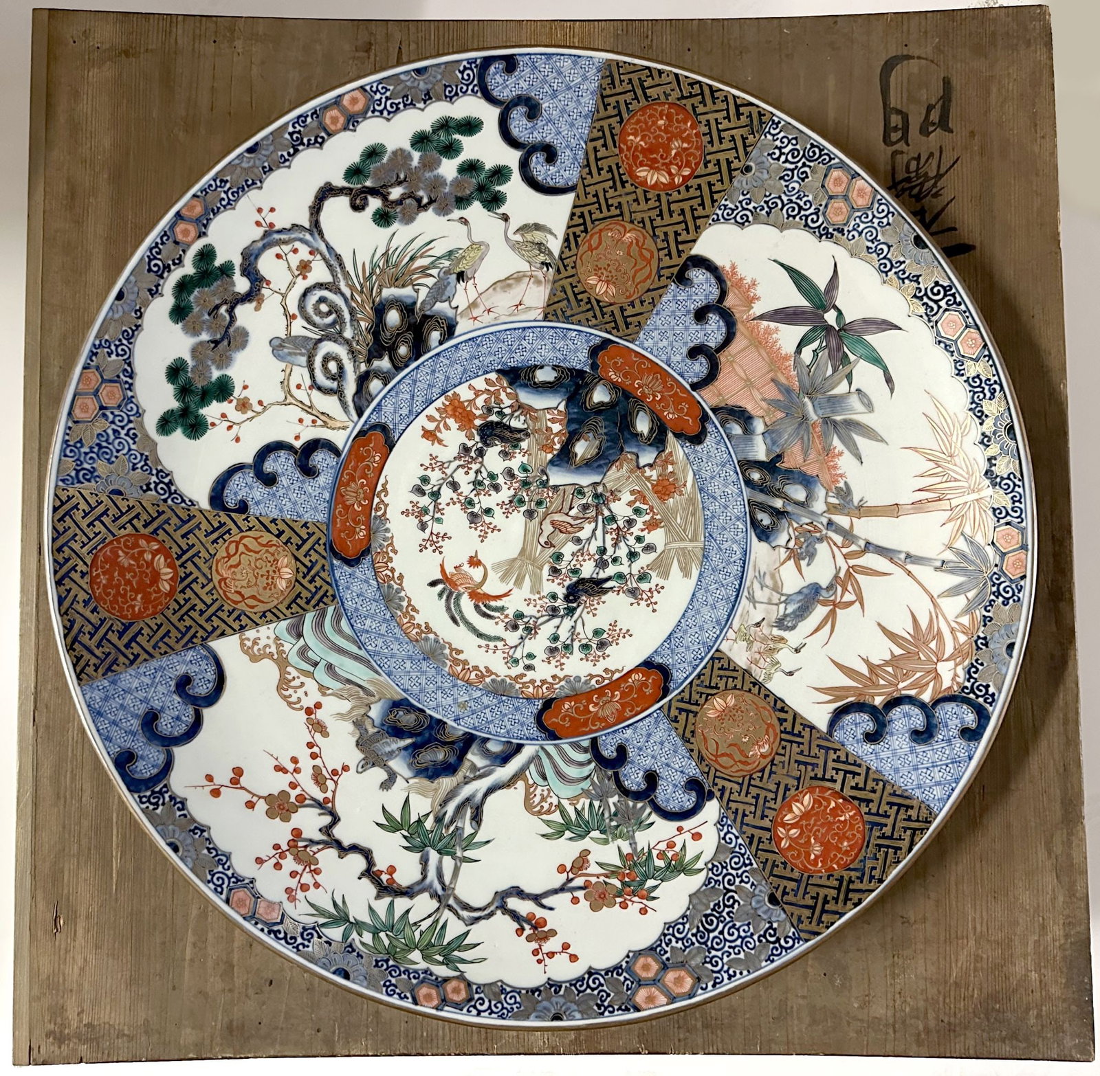 A VERY LARGE 19C. JAPANESE IMARI CHARGER WITH KIRIBAKO: The Arita kiln porcelain is decorated in underglaze blue, iron red, and gilt with fan-shaped panel reserves enclosing birds, flowering branches, and auspicious pine, bamboo, and plum motifs within geo
