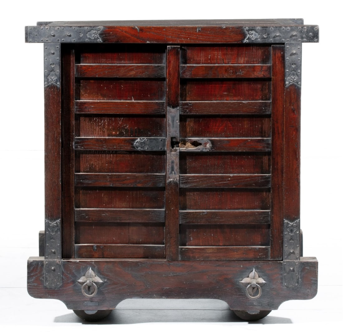 A JAPANESE KURUMA DANSU ON WHEELS CIRCA 1800: The keyaki wood and cedar mortise-and-tenon constructed case with side slatting and iron mounts has two slatted doors that open to six drawers. Measures 30.5 x 30 x 18 inches. Provenance: The estate o