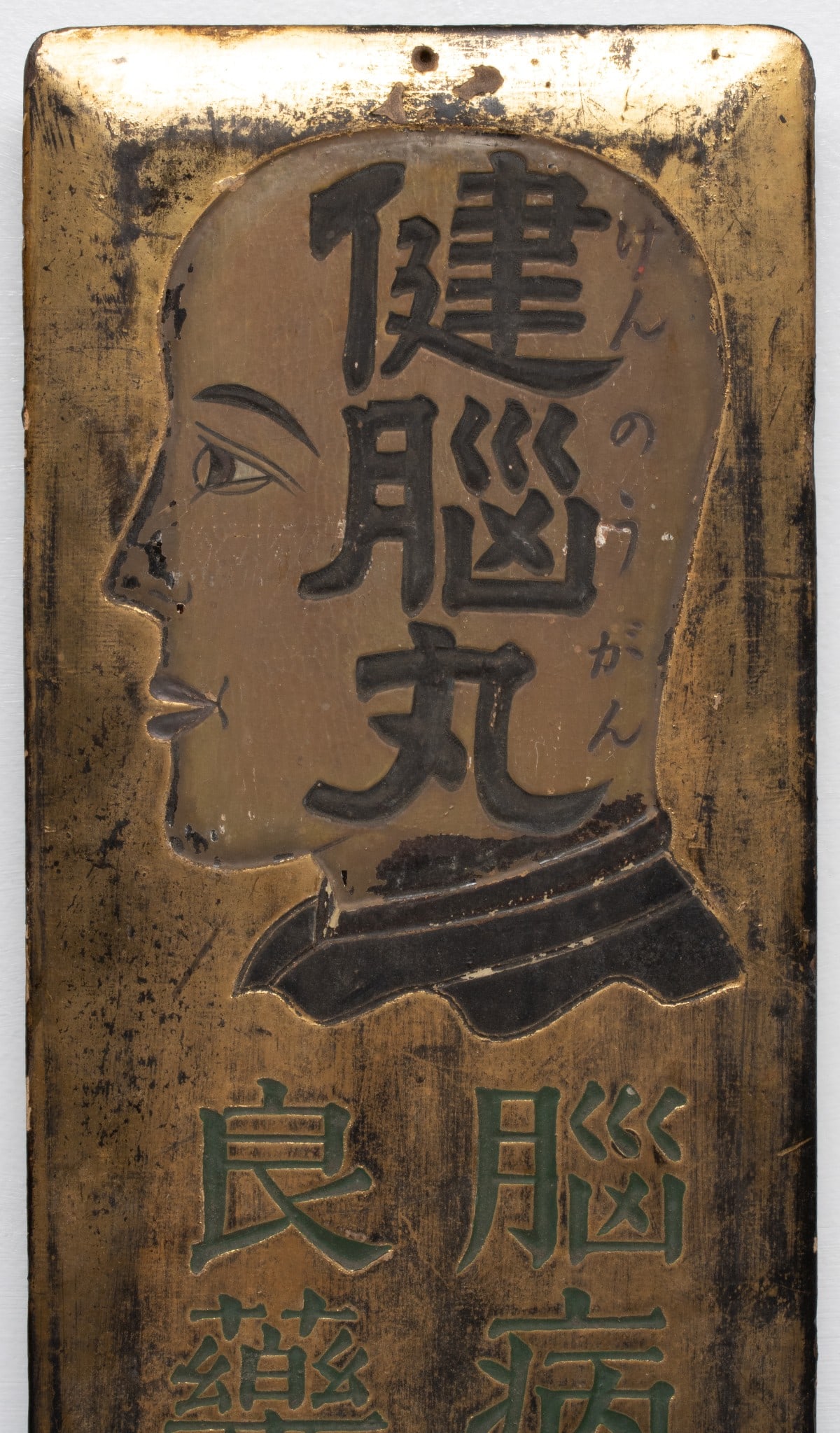 A RARE 19C. SIGN FOR THE 'BRAIN-HEALING PILL' KENNOMARU: The rare late 19th century Japanese carved wood advertising sign features a bald Buddhist monk-like man's head in profile with the words Kenno-marua in bas-relief and a lower panel with the incised wo