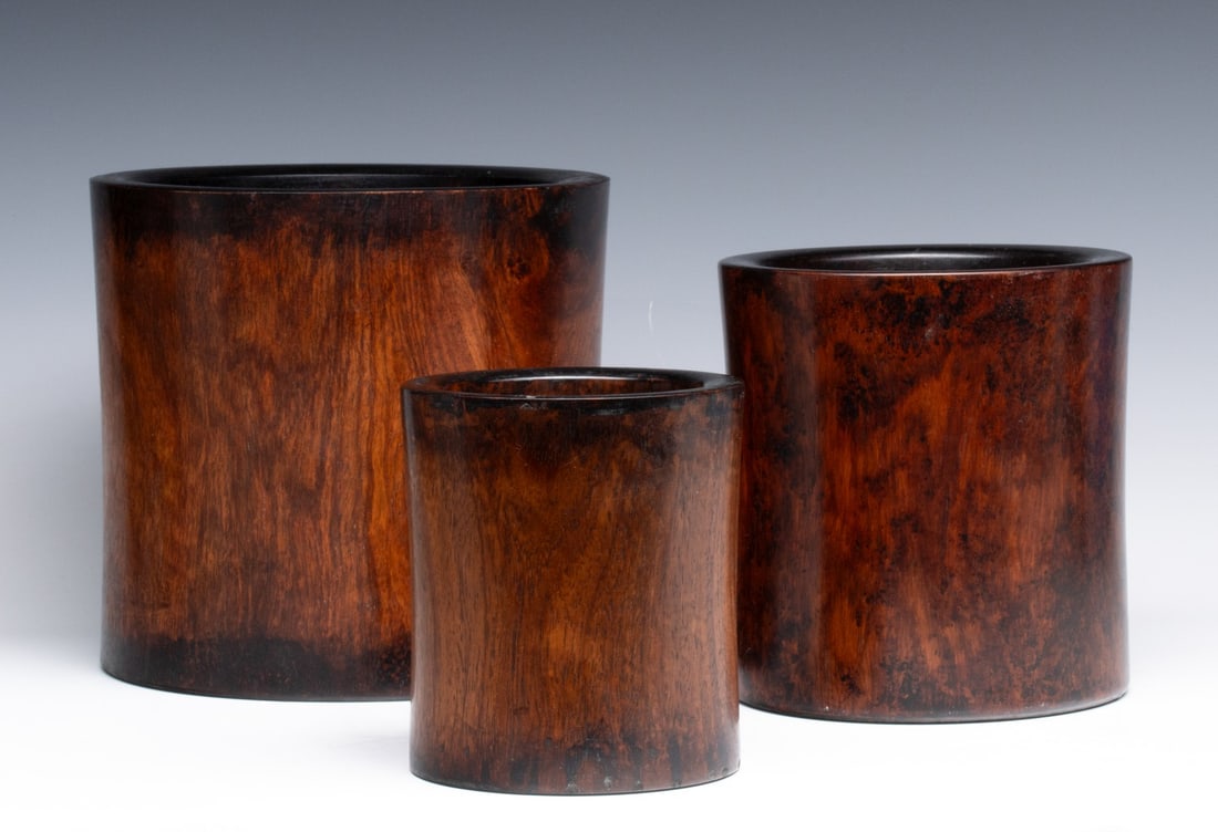 THREE ANTIQUE CHINESE HUANGHUALI TYPE BRUSH POTS: Two wood brush pots with good patina and closely matched have their original inserts, a third slightly smaller has no opening or insert. Sizes range from 5.75 x 5 to 8.25 x 8.75 inches. Provenance: Th