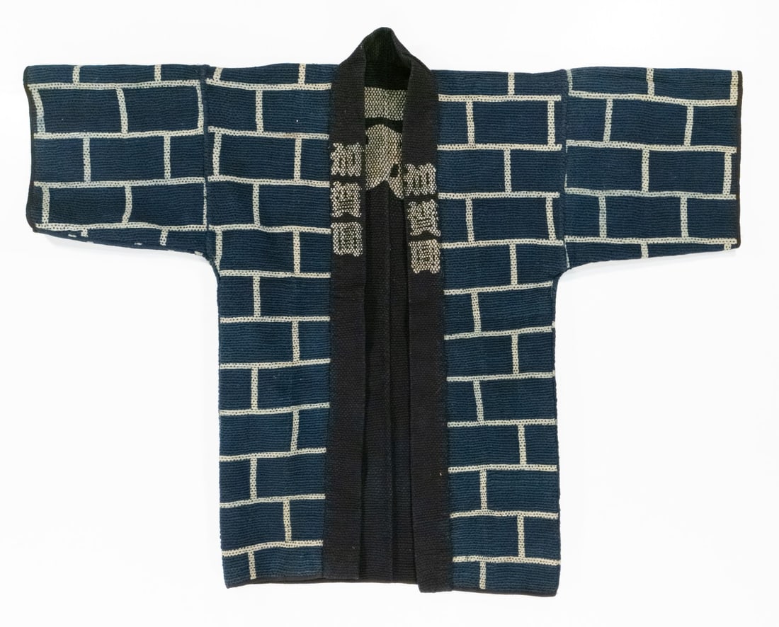 A JAPANESE BRICK MOTIF FIREMAN'S COAT, ADAIR ESTATE: The 19th century firefighter's jacket dyed in a fire-stopping brick motif with lapel inscriptions that may identify a region or brigade is constructed with multiple layers of indigo-dyed cotton densel